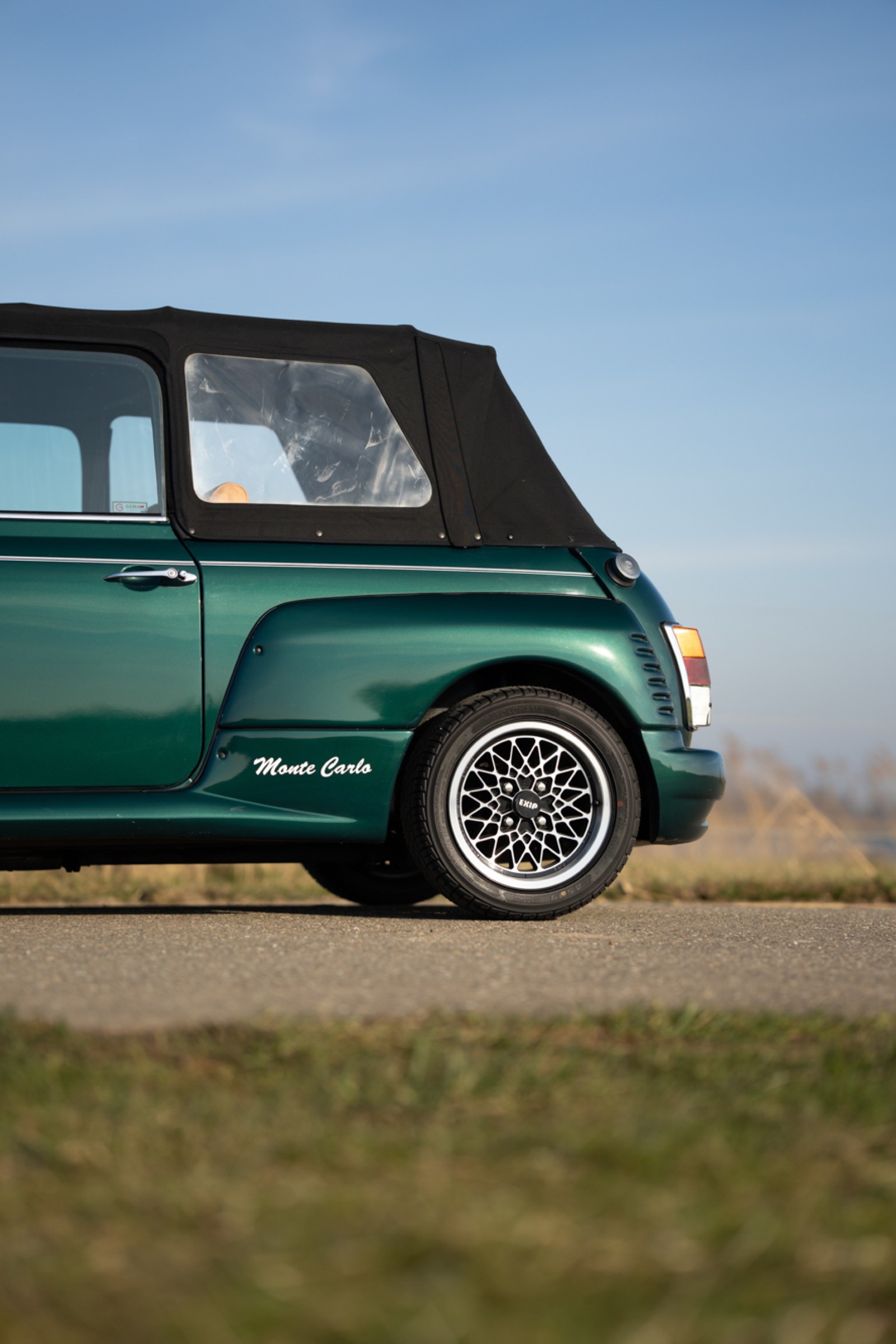 A vintage green convertible car parked on a sunny day with a clear blue sky in the background.