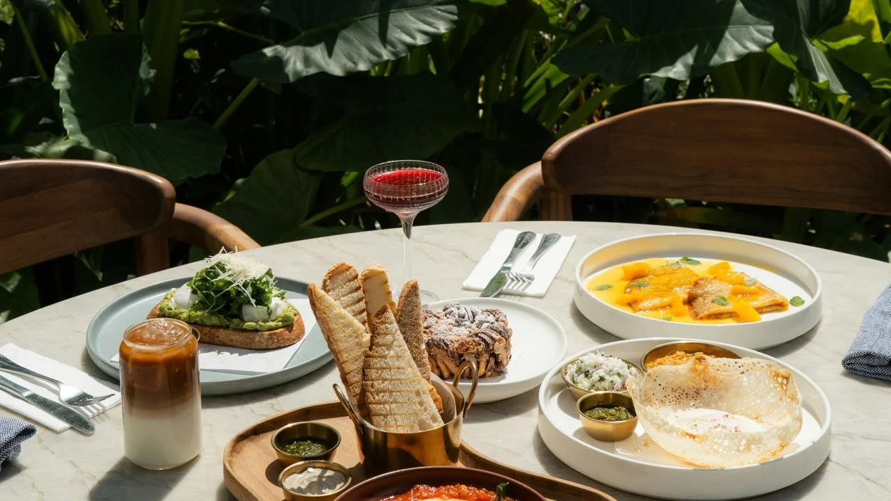 Restaurant table set with brunch plates, toast and iced coffee among tropical plants