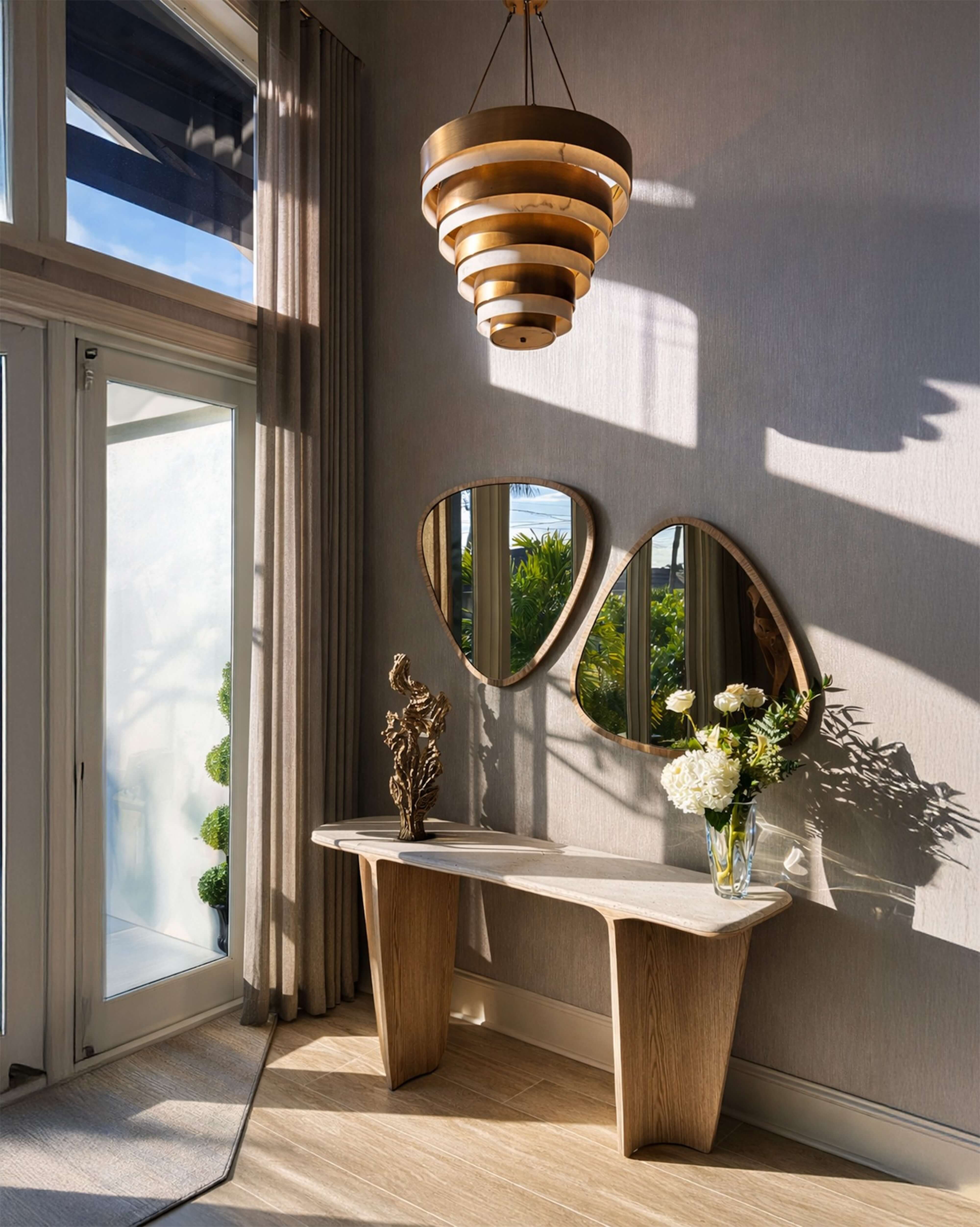 Sunlit foyer vignette with sculptural pendant, curved mirrors, marble console, and soft natural shadows.