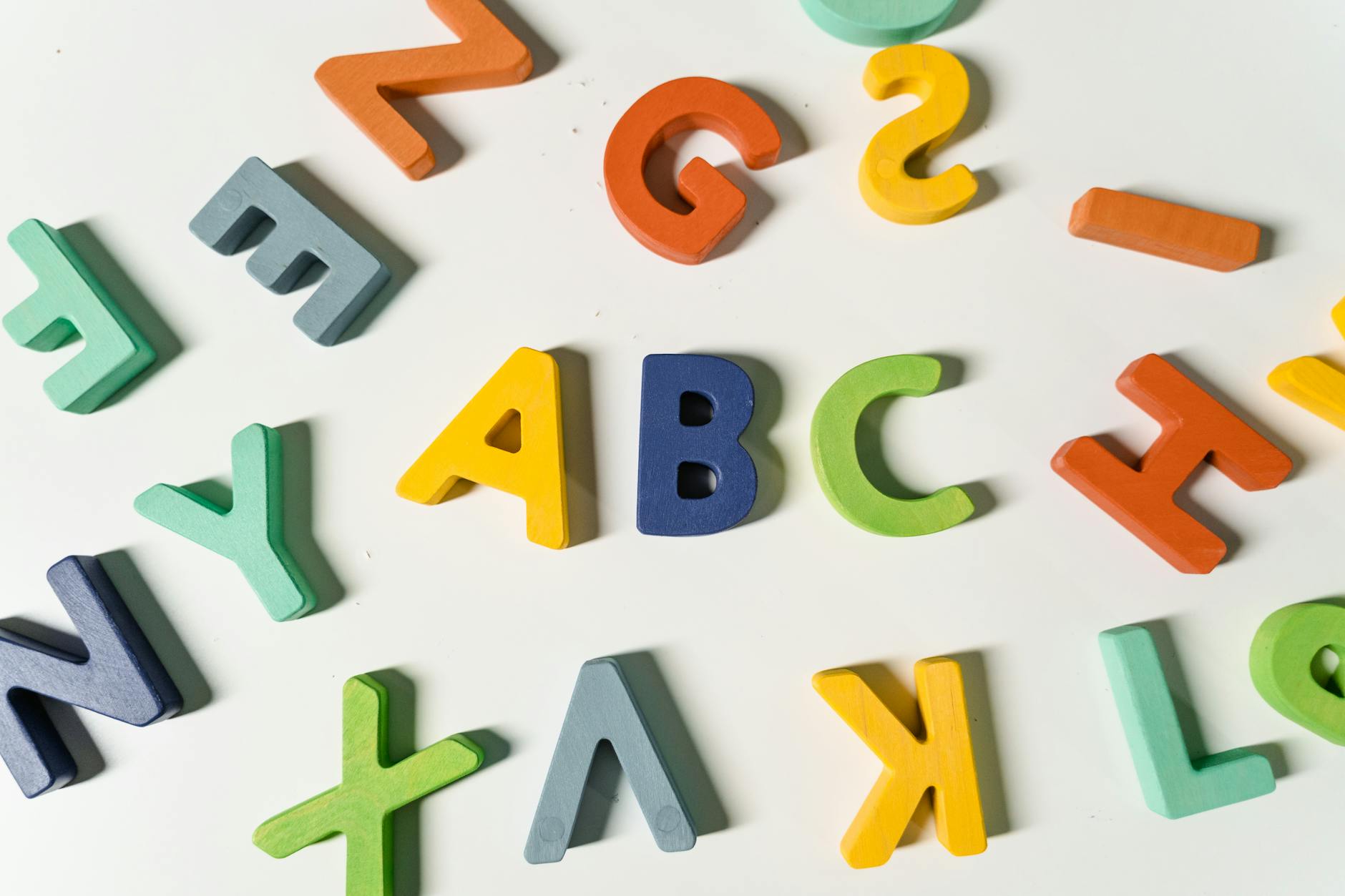 A child traces the letter B in a tray of colorful sand next to printed learning letters worksheets on the table.