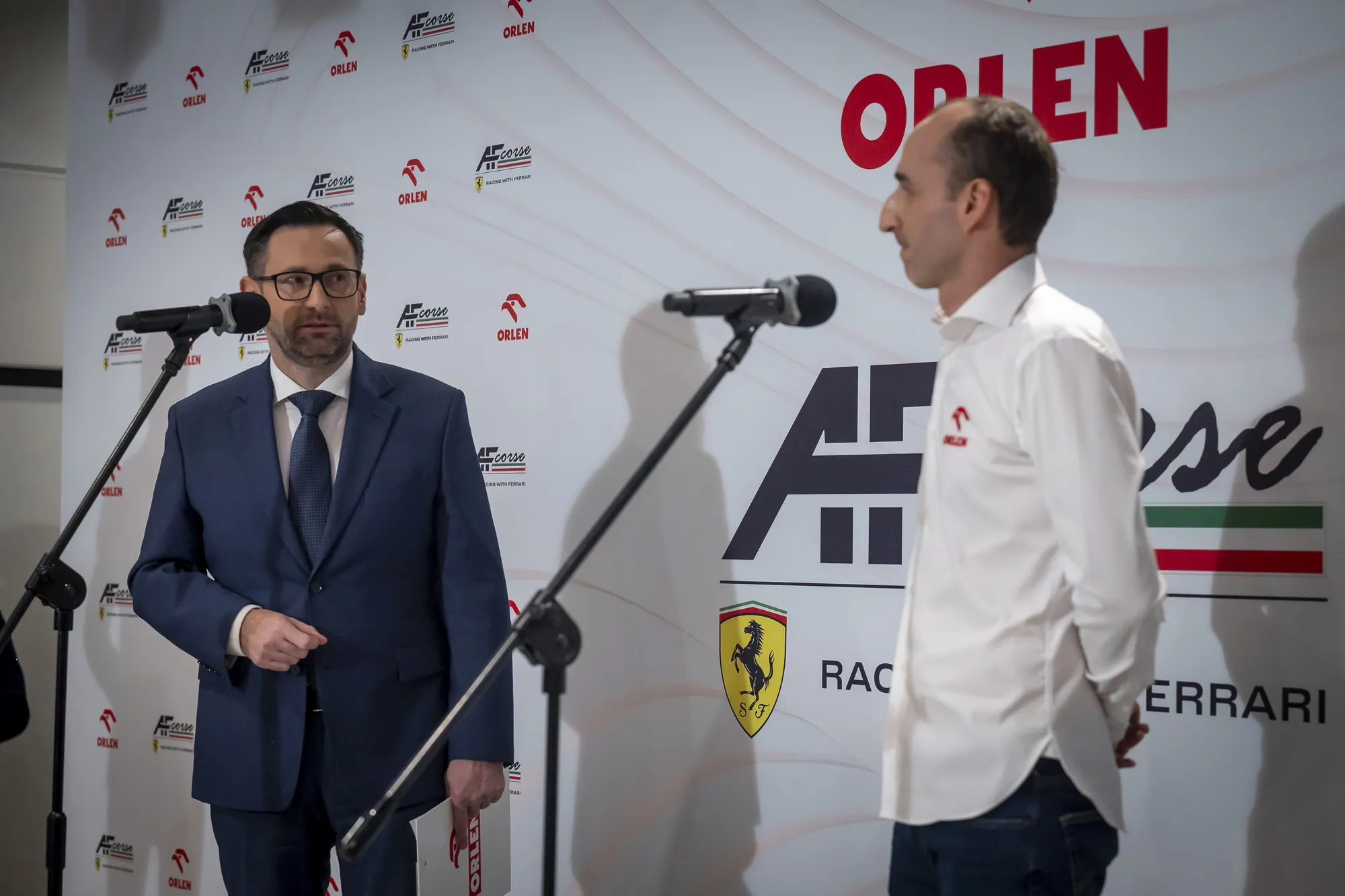 Robert Kubica podczas konferencji prasowej ORLEN na scenie z prowadzącym.