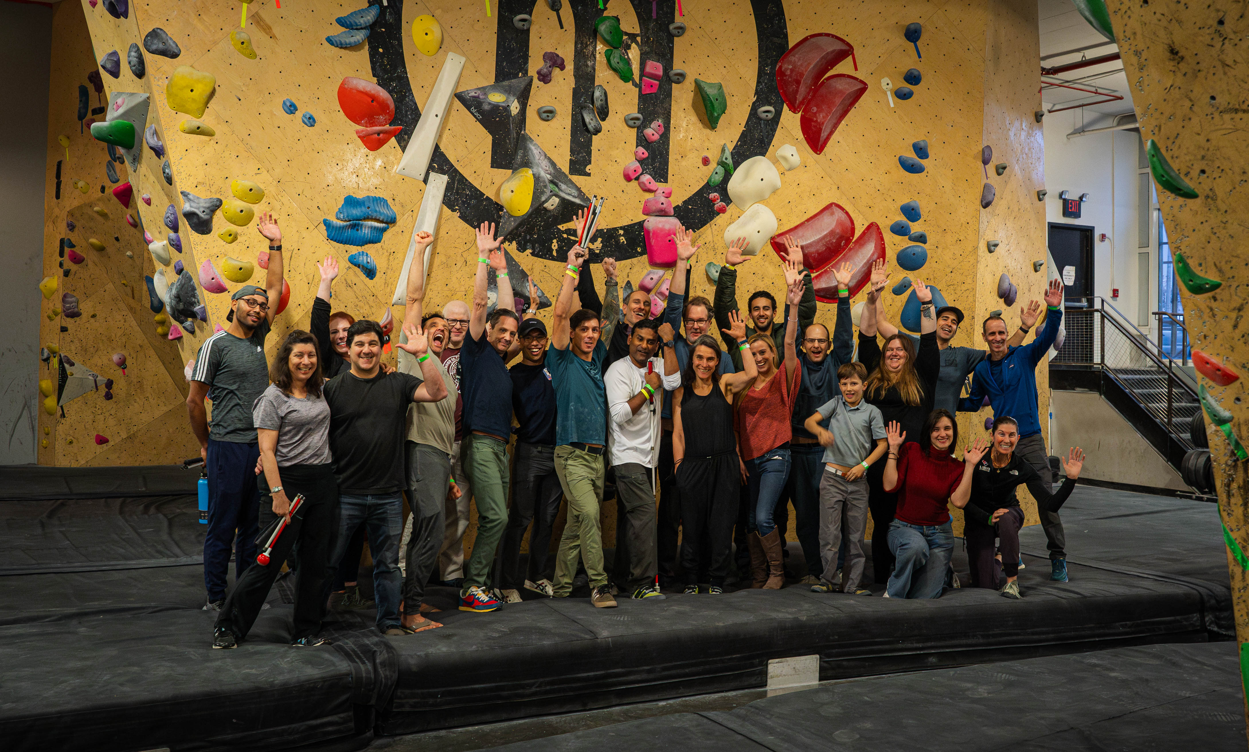 Group photo of event attendees standing inside Brooklyn Boulders climbing gym. The group celebrate with smiles and hands in the air.