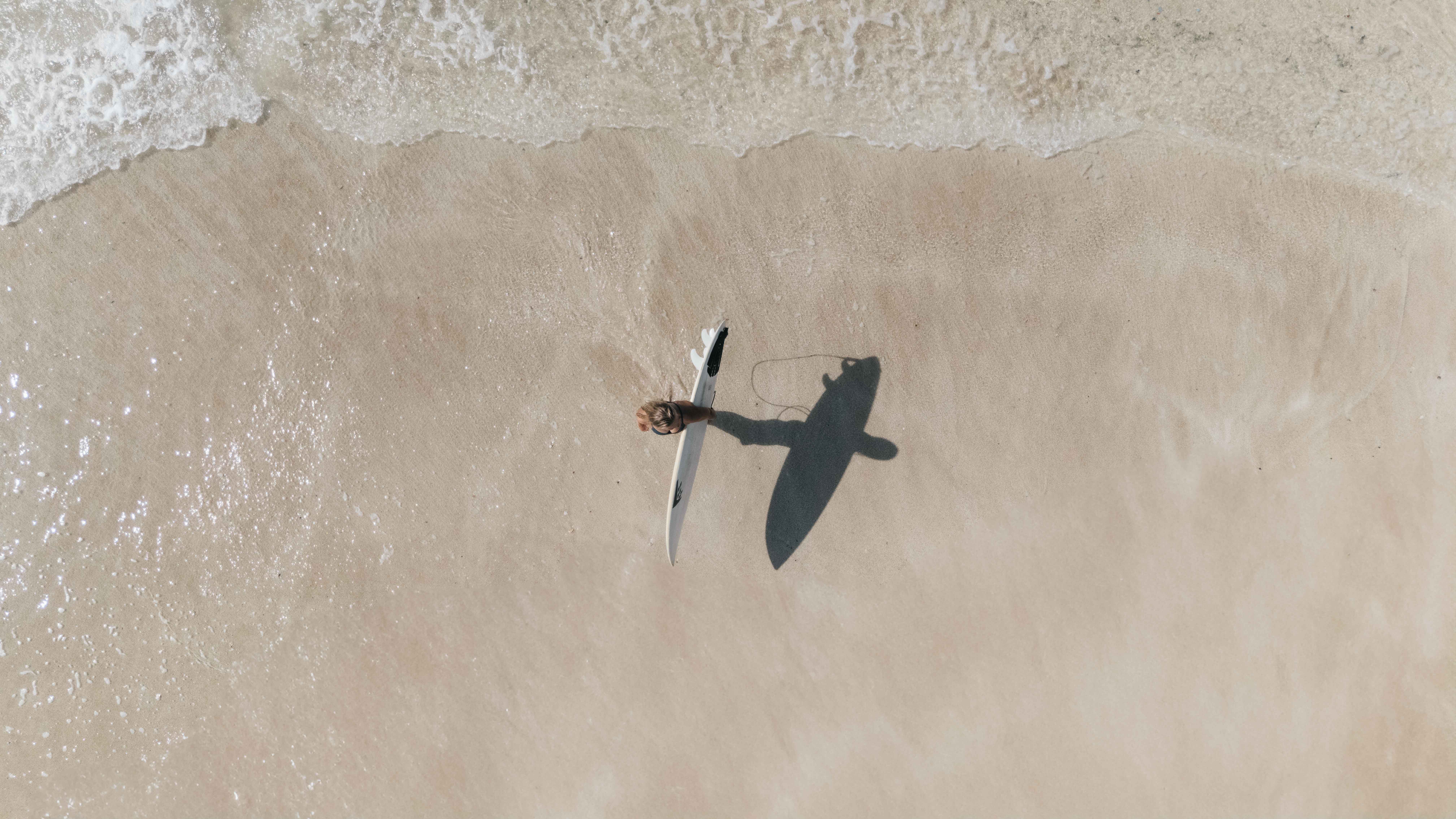 Girl standing at the beach with surf board in hand view from above with a drone