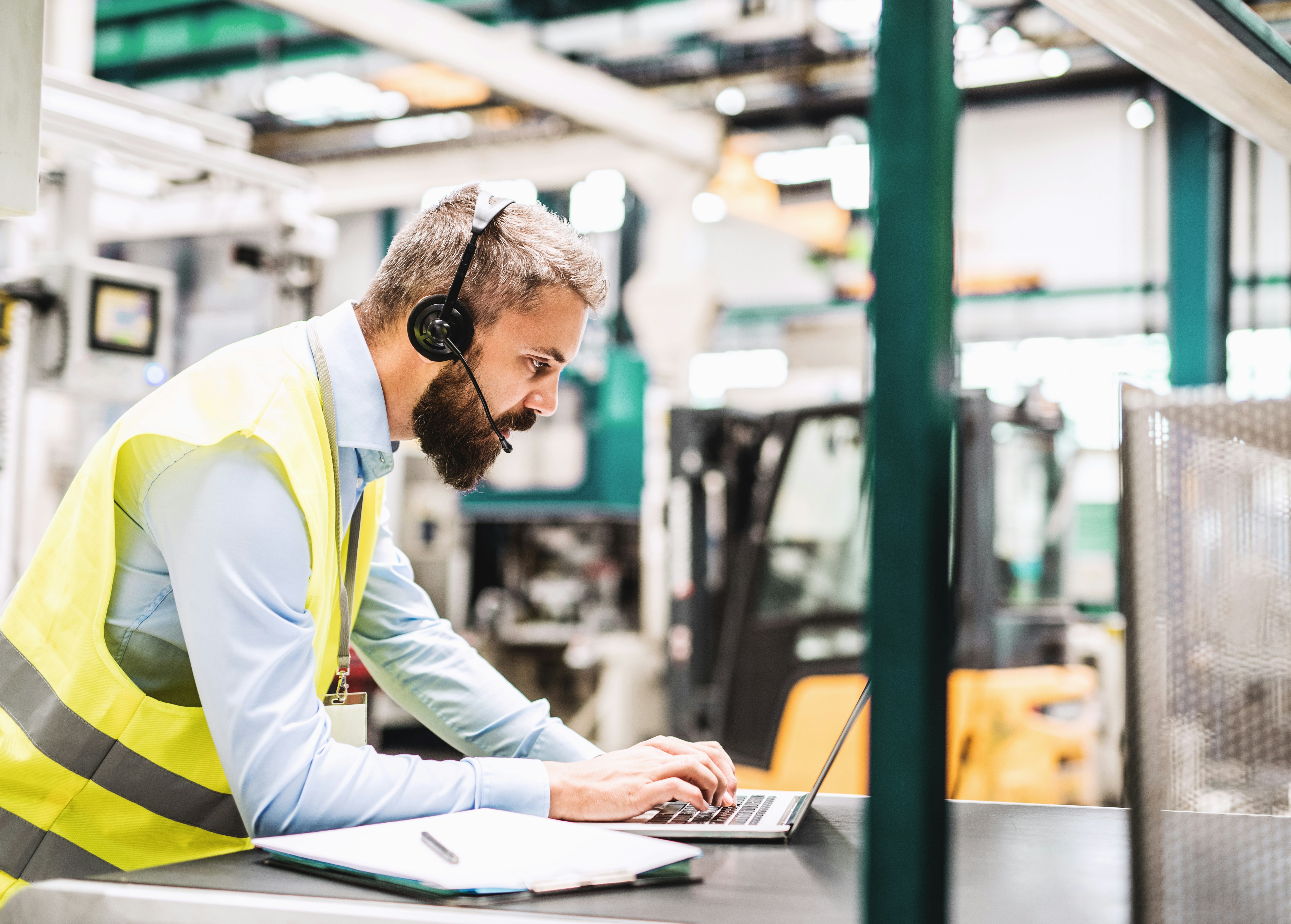 man with a headset on uses a laptop in a warehouse