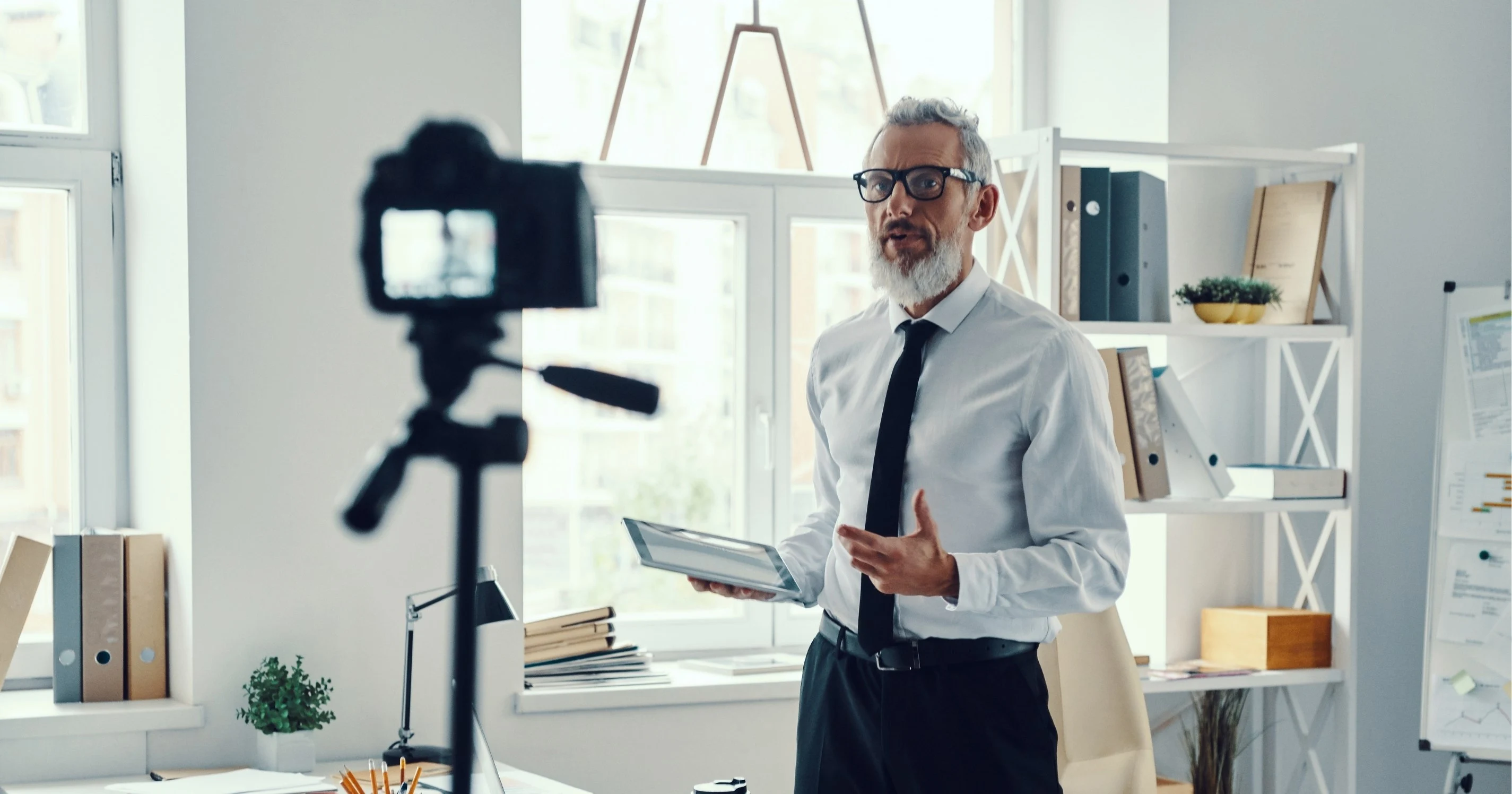 Confident mature Realtor in elegant shirt and tie telling something while making social media video