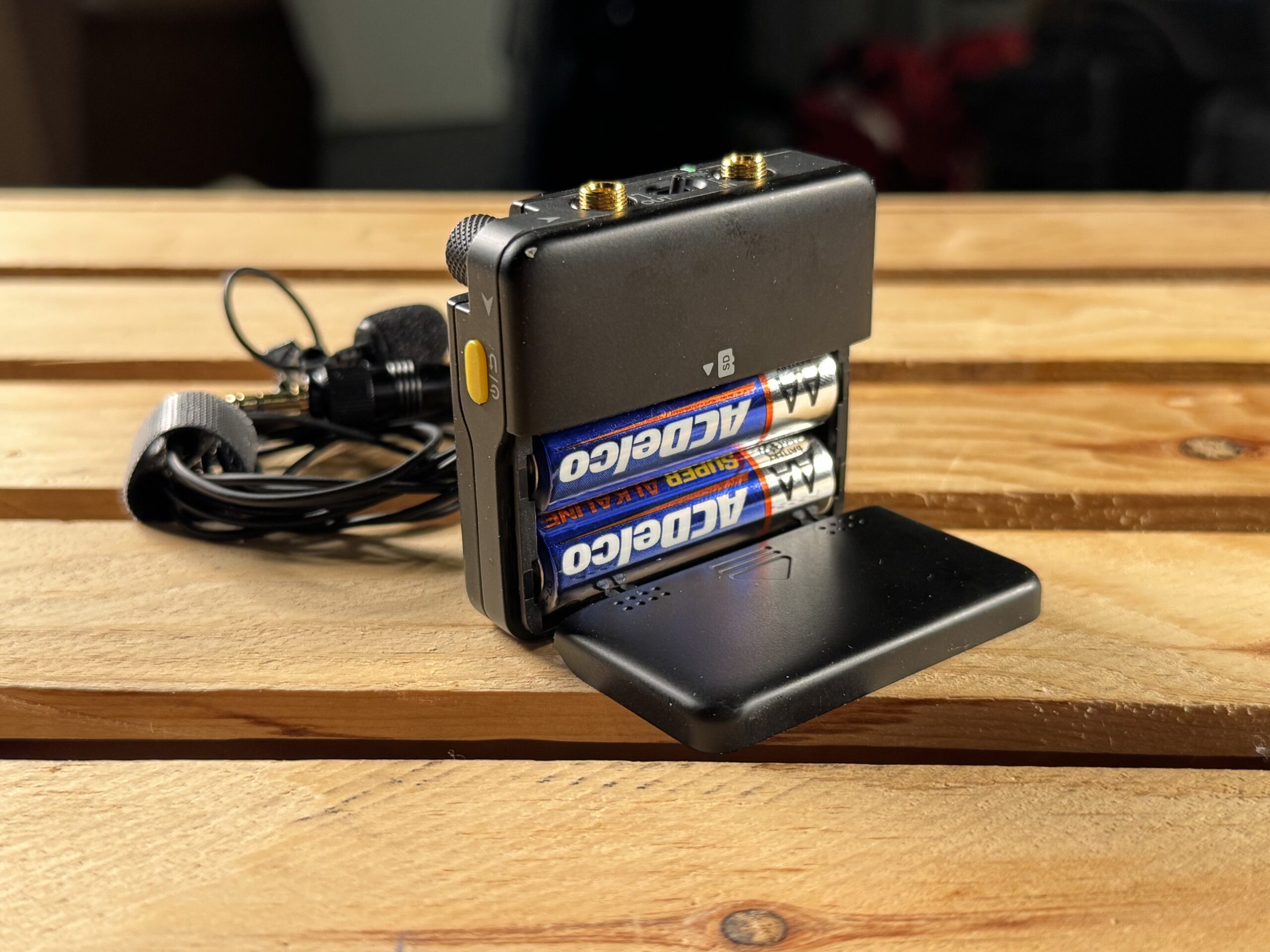 An open battery compartment on a pocket audio recorder showing two AA batteries inside.