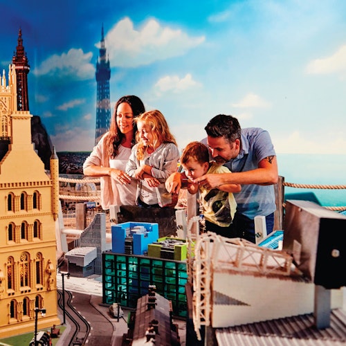 A smiling family of four admires a detailed miniature city display, featuring various buildings and landmarks.