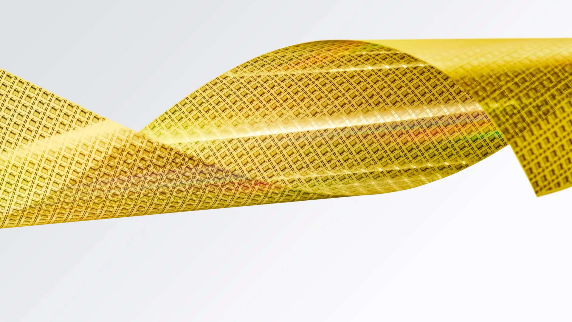 Flexible gold semiconductor wafer film twisted into a ribbon shape against a white background