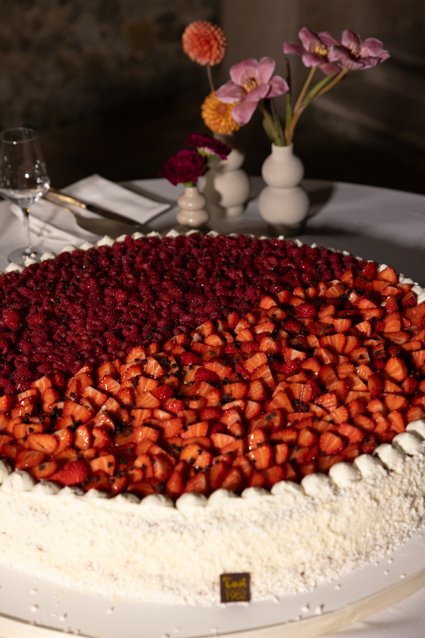 Torta matrimonio a strati con fragole e frutti rossi, fiori in vaso bianco sul tavolo ricevimento Castello Tabiano