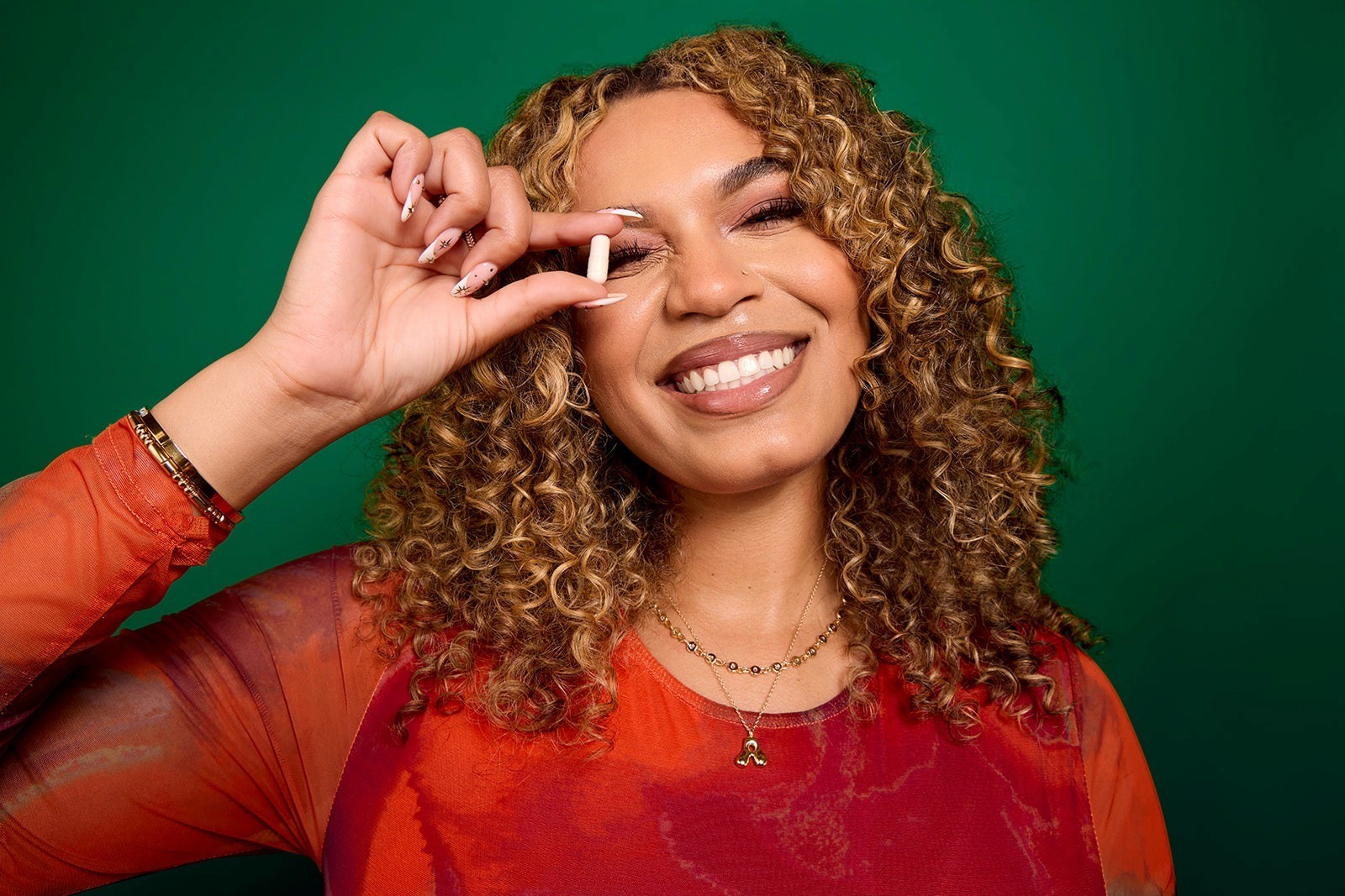 Smiling woman holding an Alori supplement capsule against a green background.