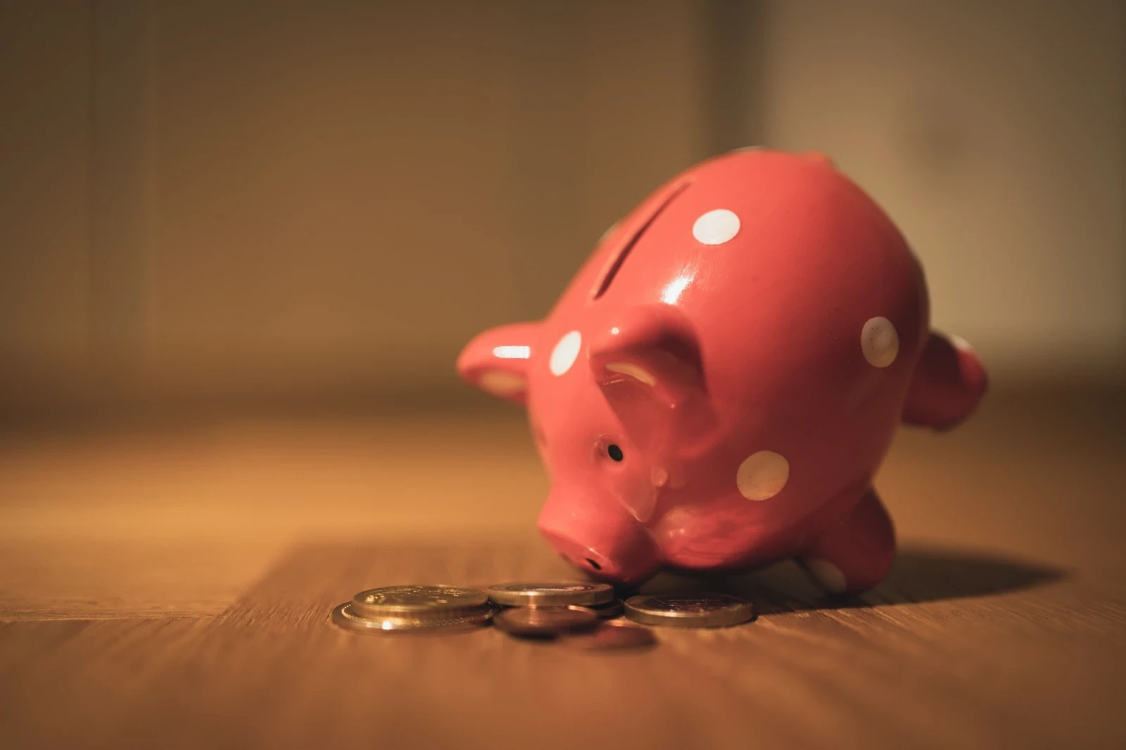 A piggy bank tilted over with all the money falling onto a wooden floor.