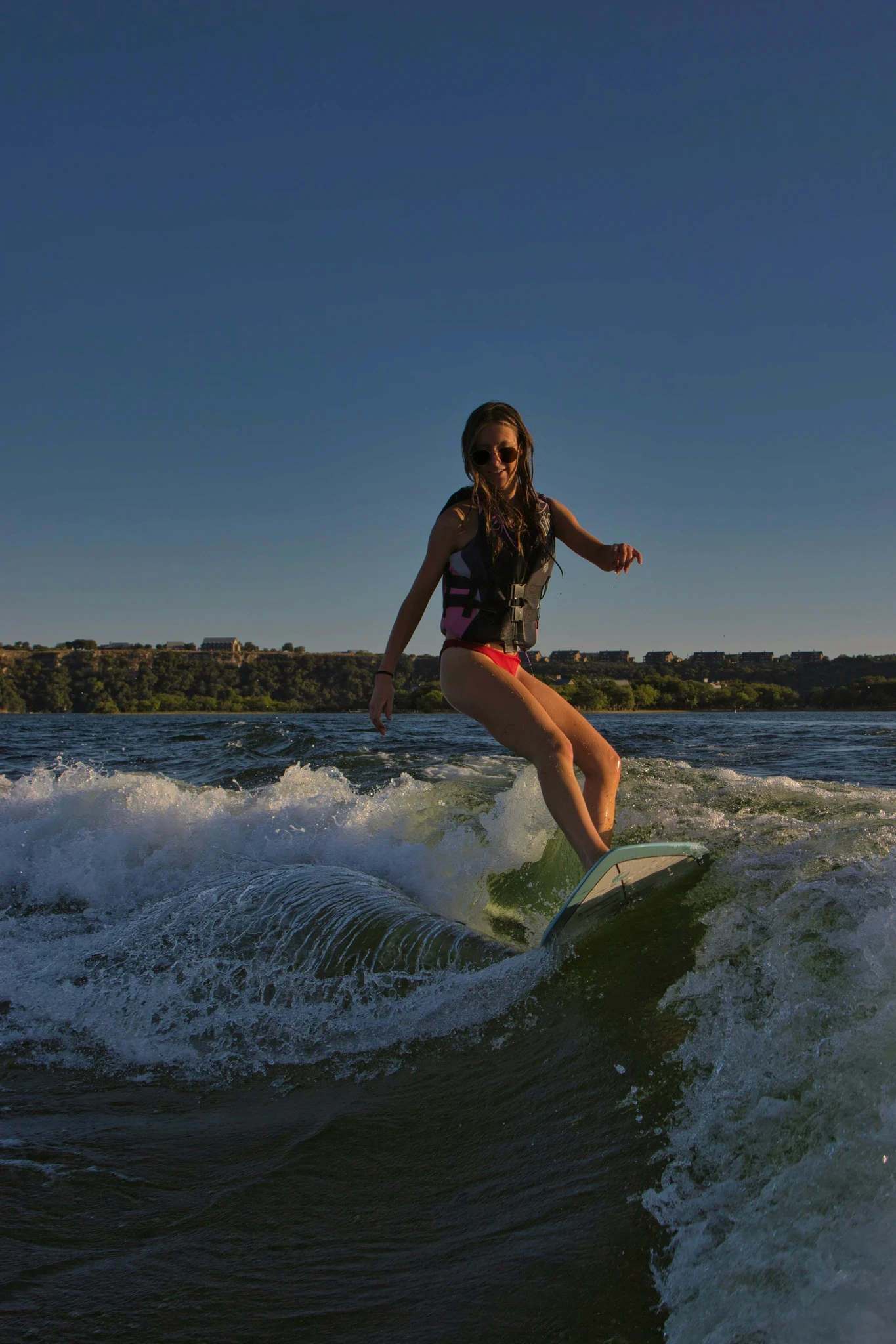 A person wearing a life vest rides a surfboard skillfully on a wave during a clear blue sky day at the lake, showcasing a balance between adventure and nature.