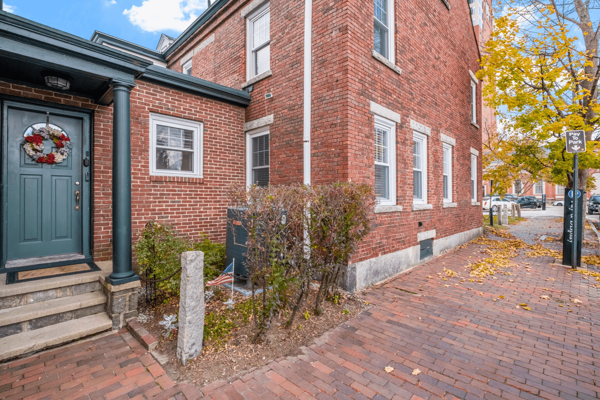 Exterior of a historic red brick vacation rental in downtown Manchester, New Hampshire, with white-trimmed windows, leafy landscaping, and a brick walkway—part of a top-grossing Airbnb in Manchester.