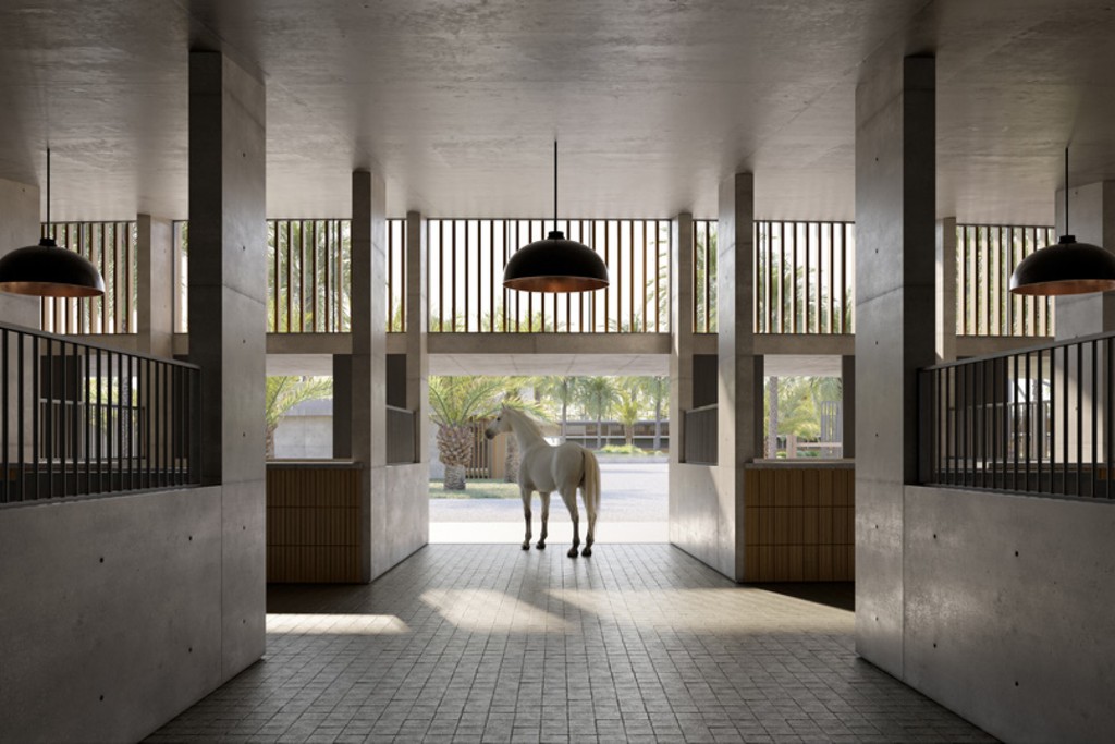  A horse stands inside Equiterra at Grand Polo, with a large window illuminating the spacious building.