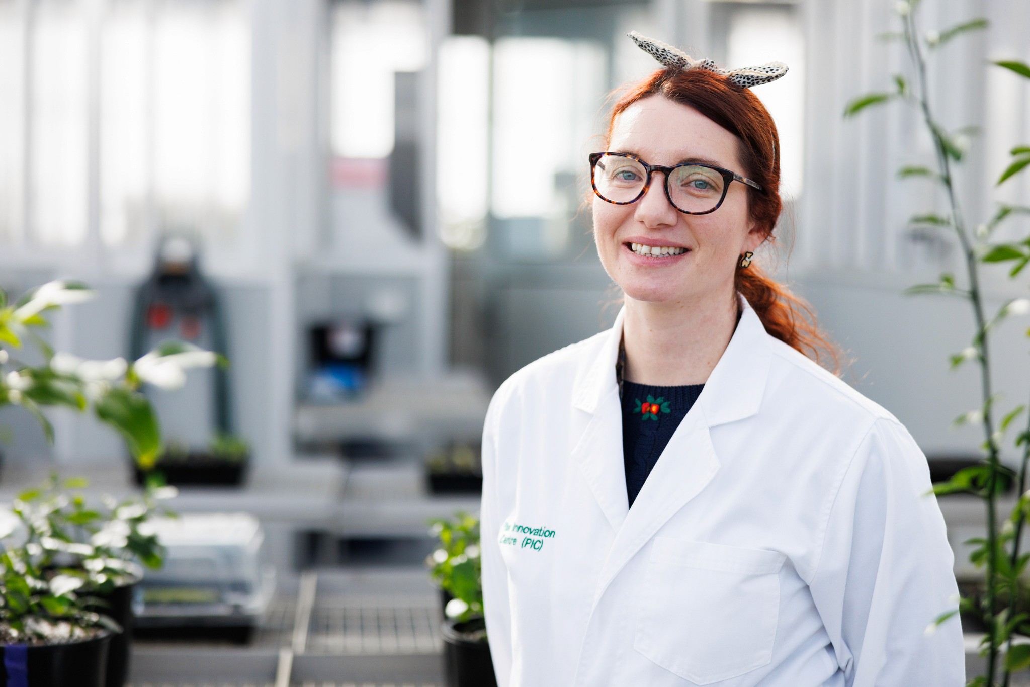 A woman stands in front of a greenhouse