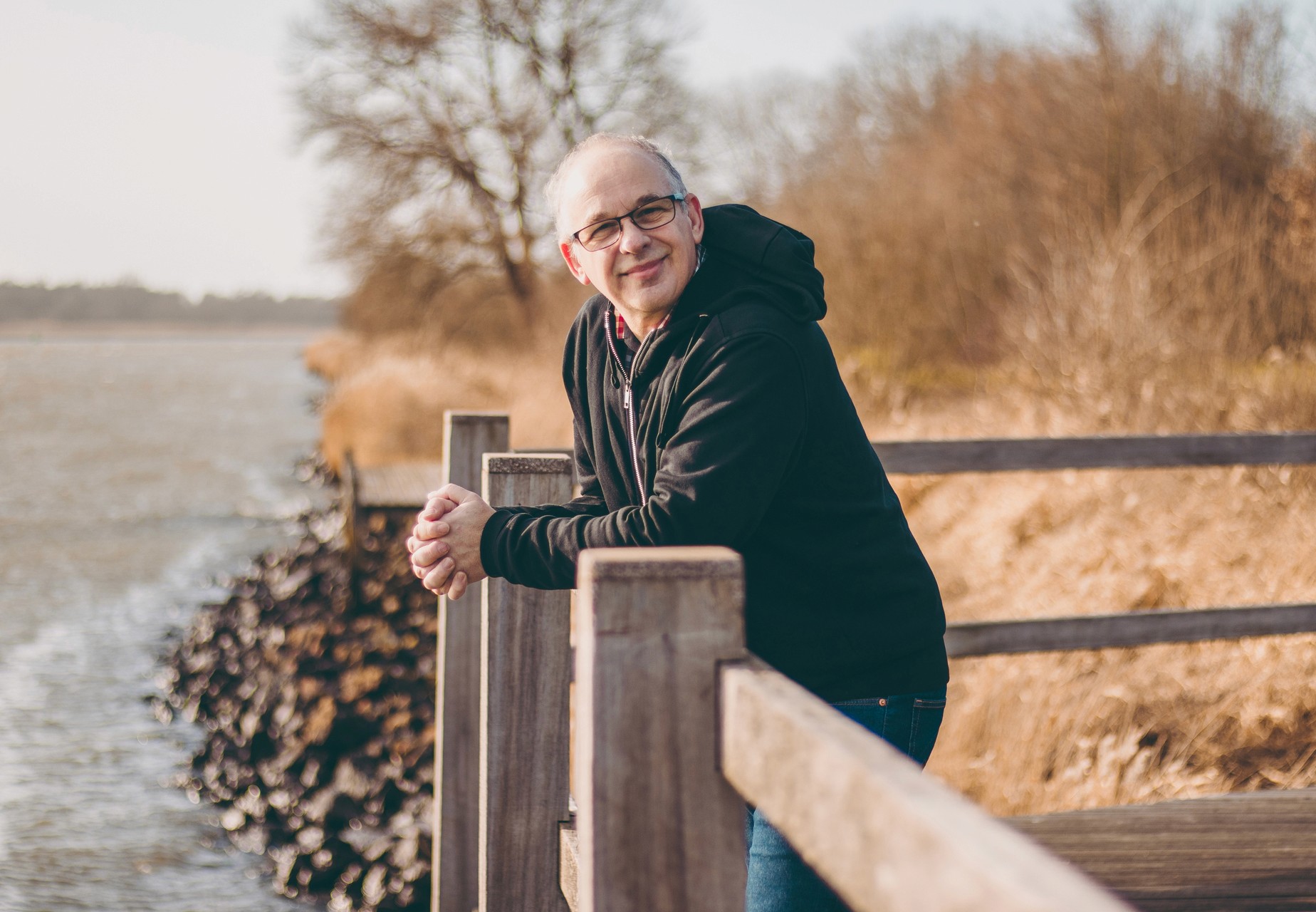 Foto van Jan Meeusen, coach leunt ontspannen op een hek langs de waterkant.