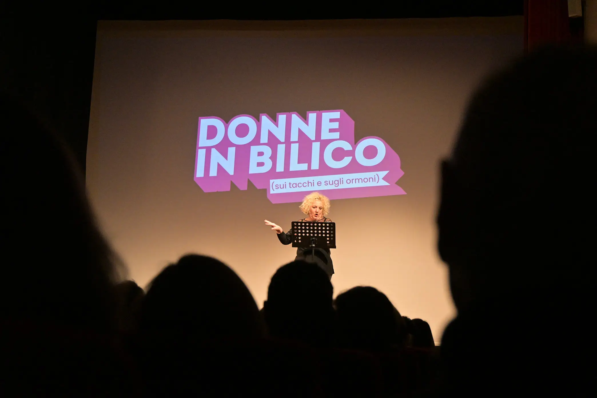 Maria Pia Timo sul palco del teatro verdi di Forlimpopoli con logo Donne in Bilico proiettato a schermo