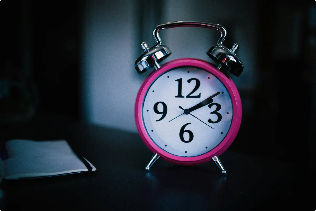 A pink alarm clock displays the time, set against a dark background with a hint of light.