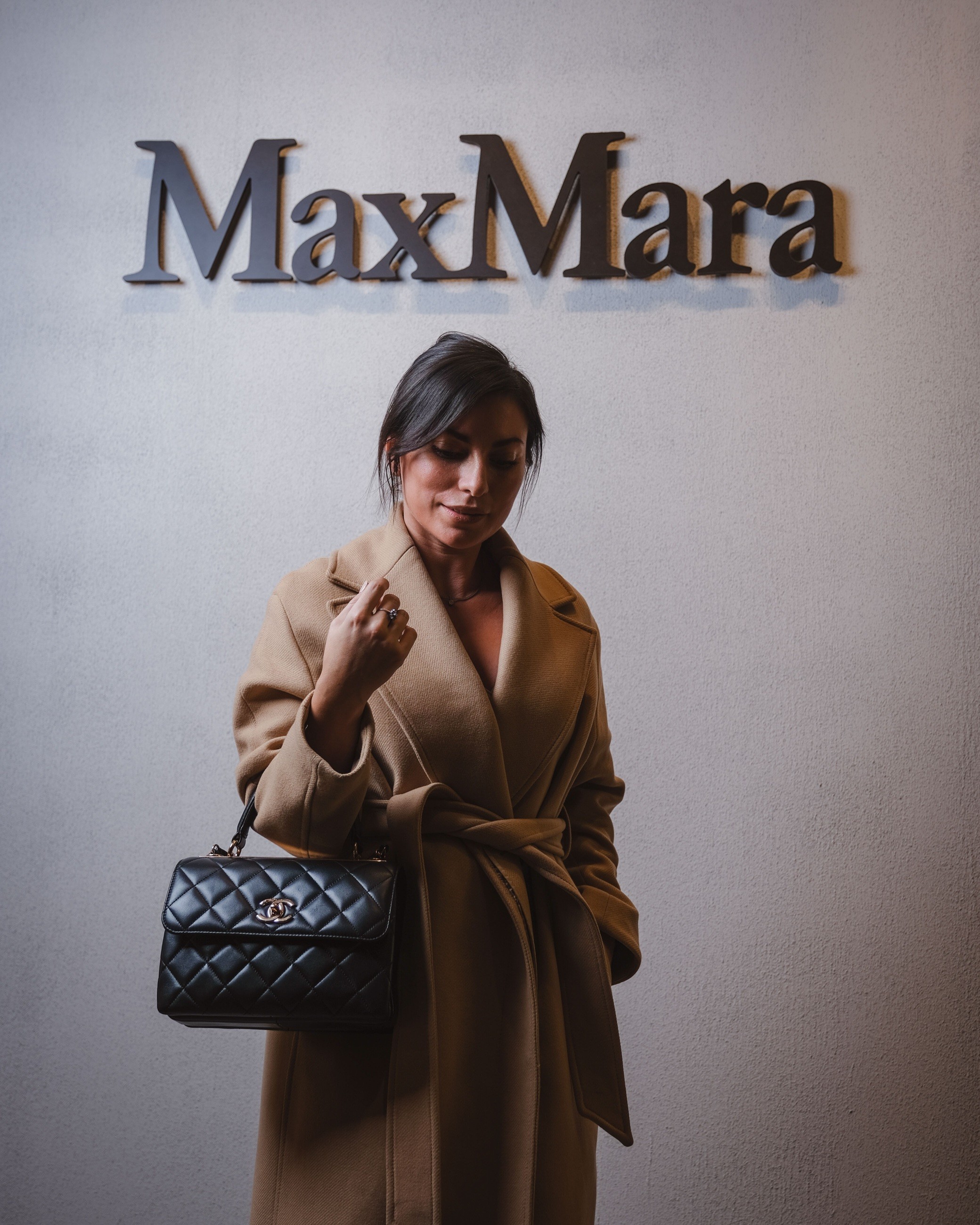 Guest in a camel coat holding a black quilted handbag at the Max Mara event