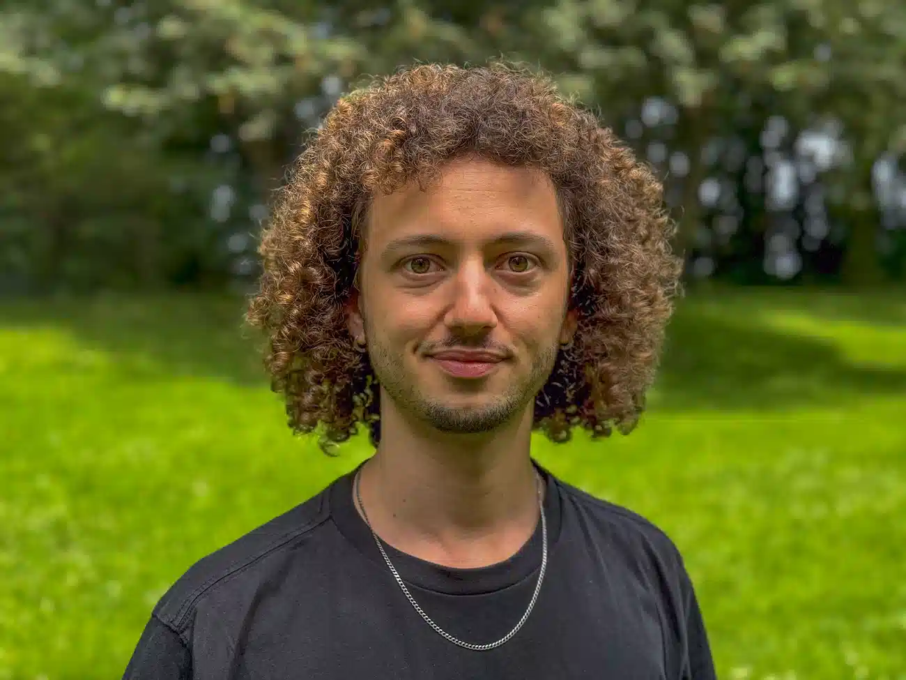 Portrait of Thiago Calderaro, Co-Founder and CEO of CoachingArea, standing in a green outdoor setting. Thiago, a UEFA B-level coach, leverages years of coaching experience and his close connection to the target audience to lead product development, marketing, and sales initiatives for the platform.