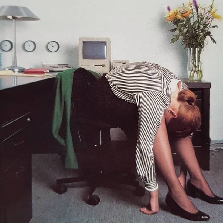 A person stretches under a desk near a vintage Mac and wall clocks, poking fun at backup setup hassle