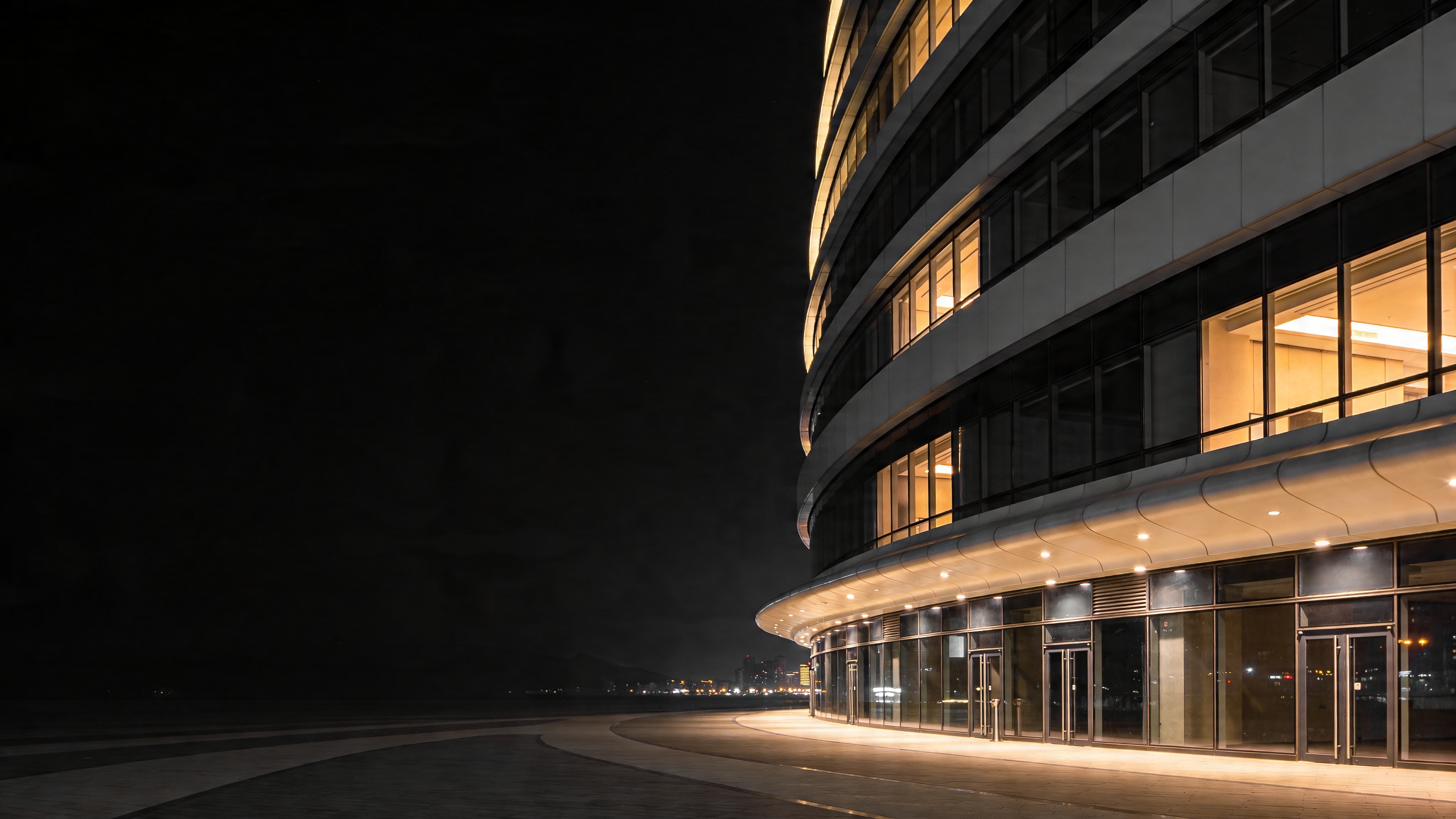 Modern curved glass office building at night with warm interior lighting and dramatic dark surroundings