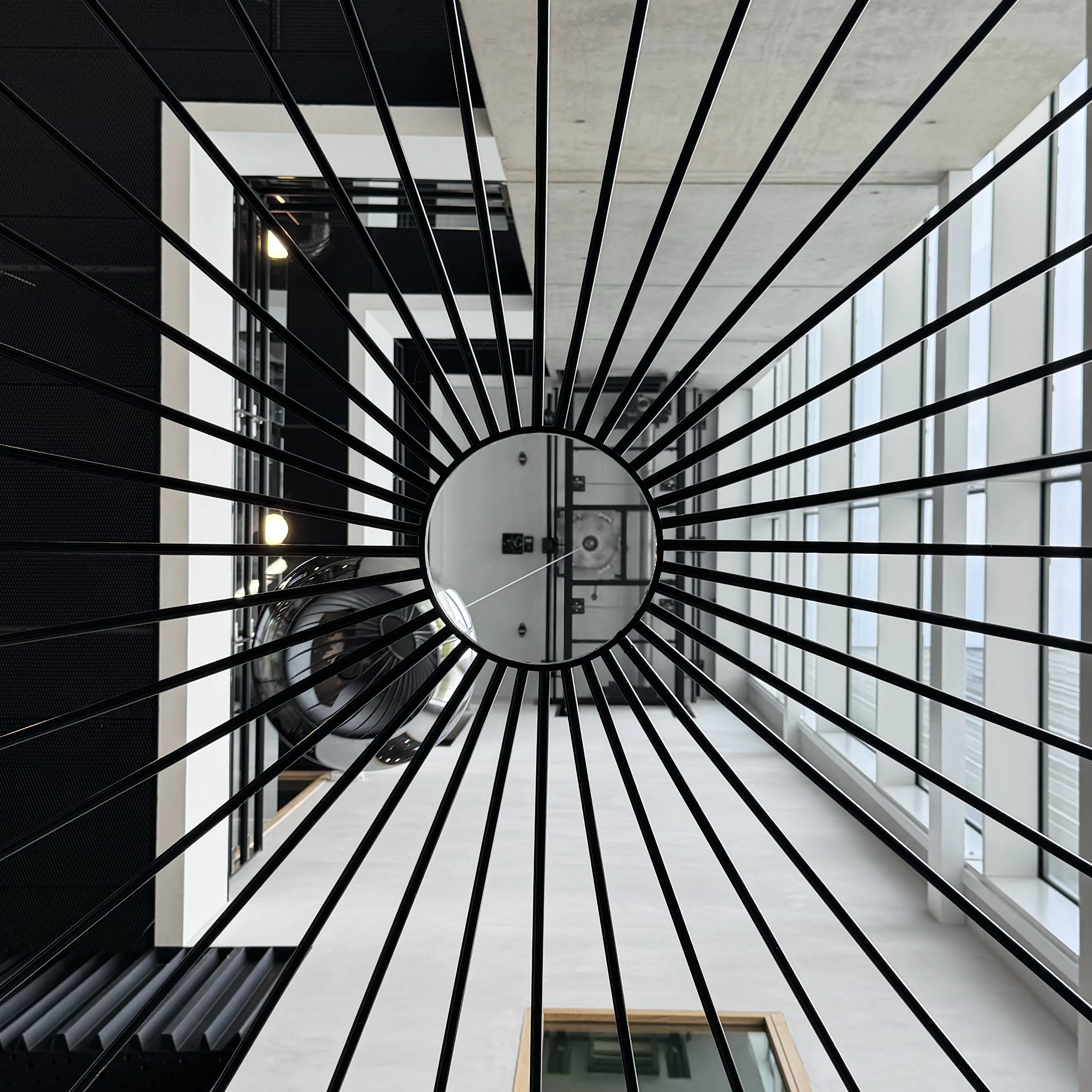 Pendule sphérique suspendu dans le hall de Cosmocité, un centre scientifique moderne aux structures métalliques élancées et aux grandes baies vitrées. L'objet décoratif, de forme ronde et lisse, contraste avec l'architecture géométrique et lumineuse du bâtiment.