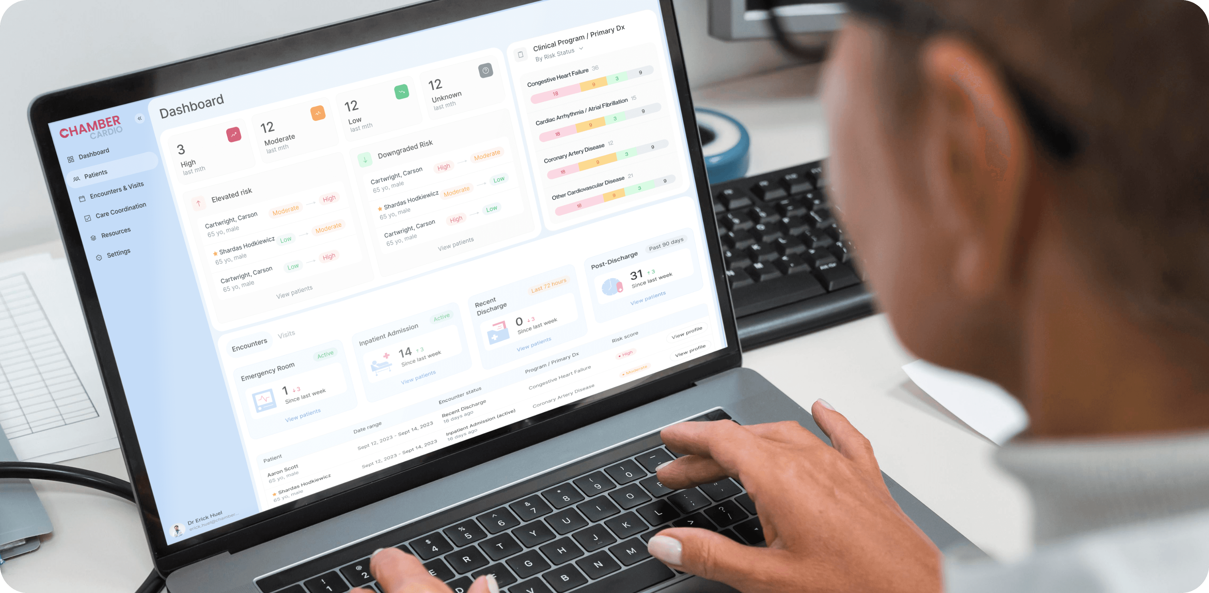 A close-up image of a person using a laptop displaying a health management dashboard. The interface on the screen belongs to ChamberCardio and is organized into various sections, including: Risk Levels: "High," "Moderate," "Low," and "Unknown" categories for patients based on their clinical data. Encounters and Visits: Tracking recent visits to the emergency room, inpatient admissions, and discharges. Clinical Program/Primary Diagnosis: Monitoring conditions such as "Congestive Heart Failure," "Coronary Artery Disease," and other cardiovascular diseases. The dashboard provides a clear, organized overview of patient data, enabling healthcare professionals to monitor risks and patient encounters efficiently. The layout is user-friendly with soft colors, charts, and labeled sections, emphasizing the use of technology in healthcare management.
