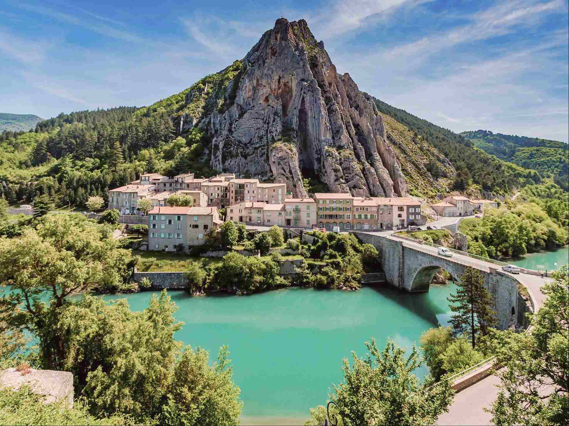 Vue du village de Castellane situé dans les Gorges du Verdon en France. On distingue le Roc de Castellane surmonté de la chapelle Notre-Dame du Roc, dominant des maisons provençales, un pont en pierre et la rivière Verdon aux eaux turquoise.