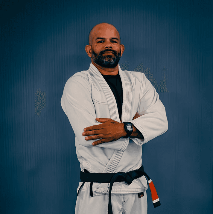 Tony “Ourico” in a white gi with arms crossed, standing confidently in front of a blue background