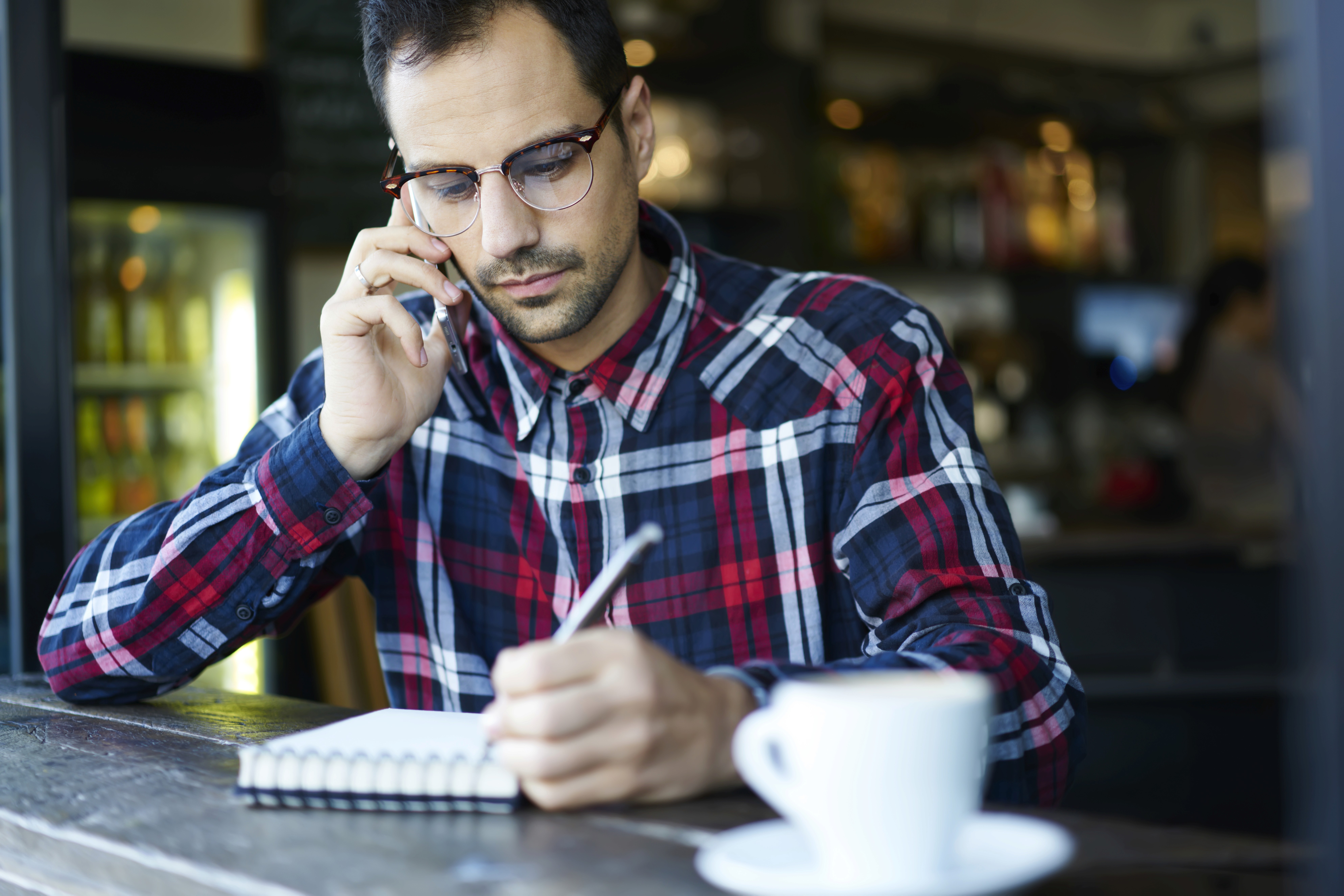 man die aan de telefoon zit terwijl in een notitieboek schrijft in een cafe