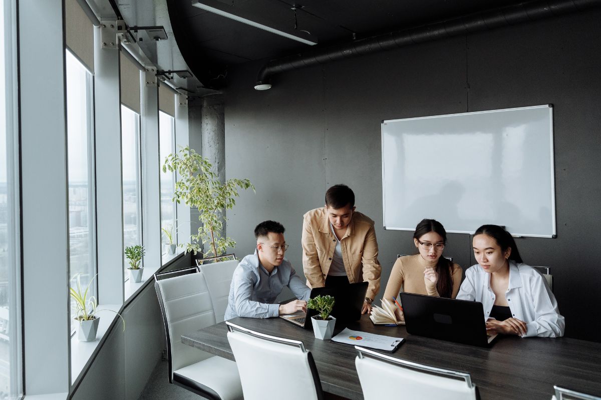 People sitting in a large office with computers and plants.