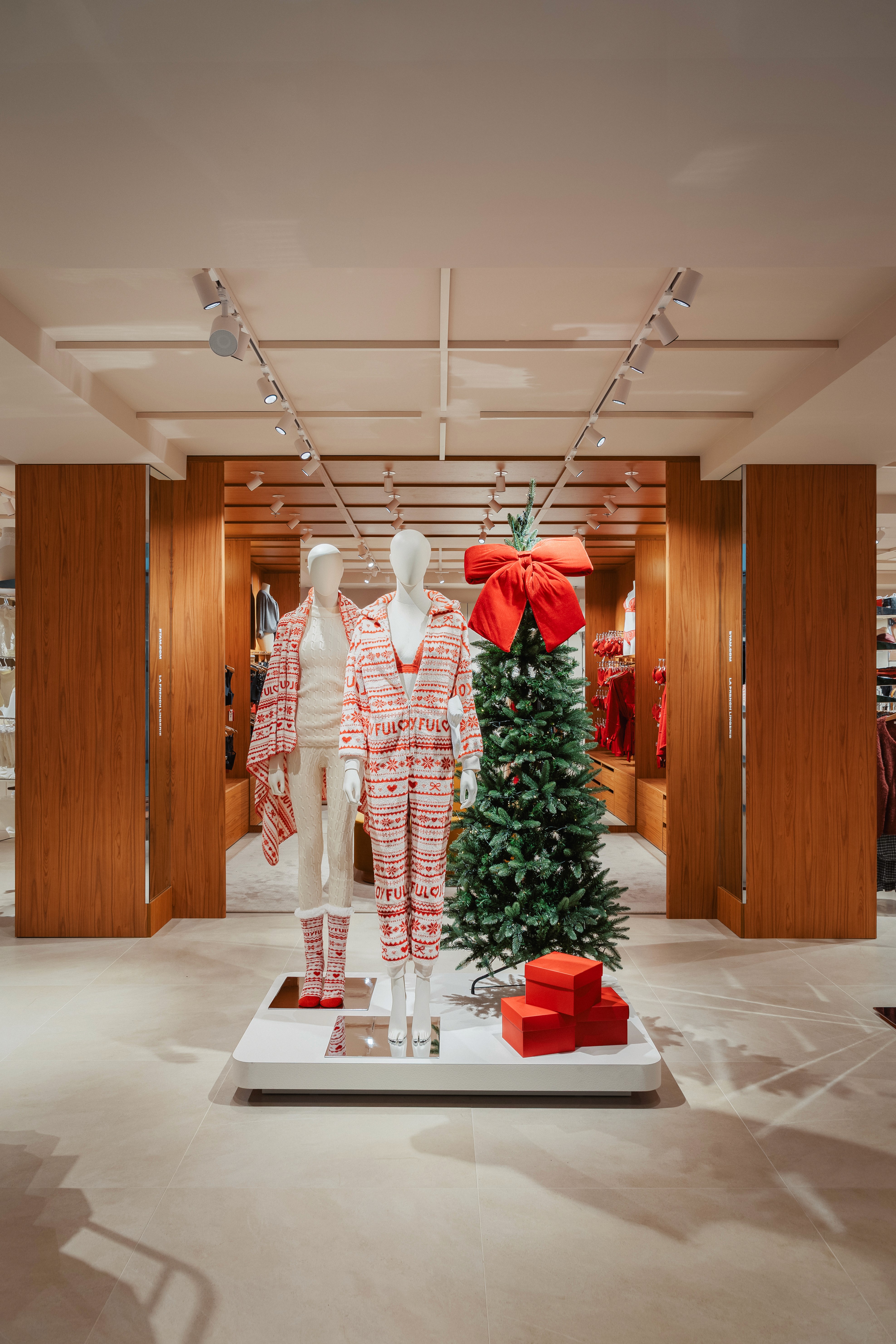 Deux mannequins en pyjamas festifs rouges et blancs, sapin décoré d’un grand nœud rouge, cadeaux aux pieds