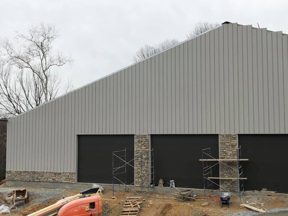 A large, gray building with a peaked roof, featuring two dark garage doors at the front, under construction.