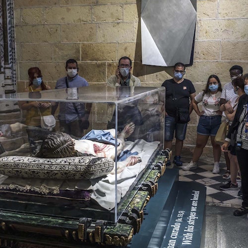 A group of people stand around a glass case containing a statue of a reclining figure, inside a historic building.