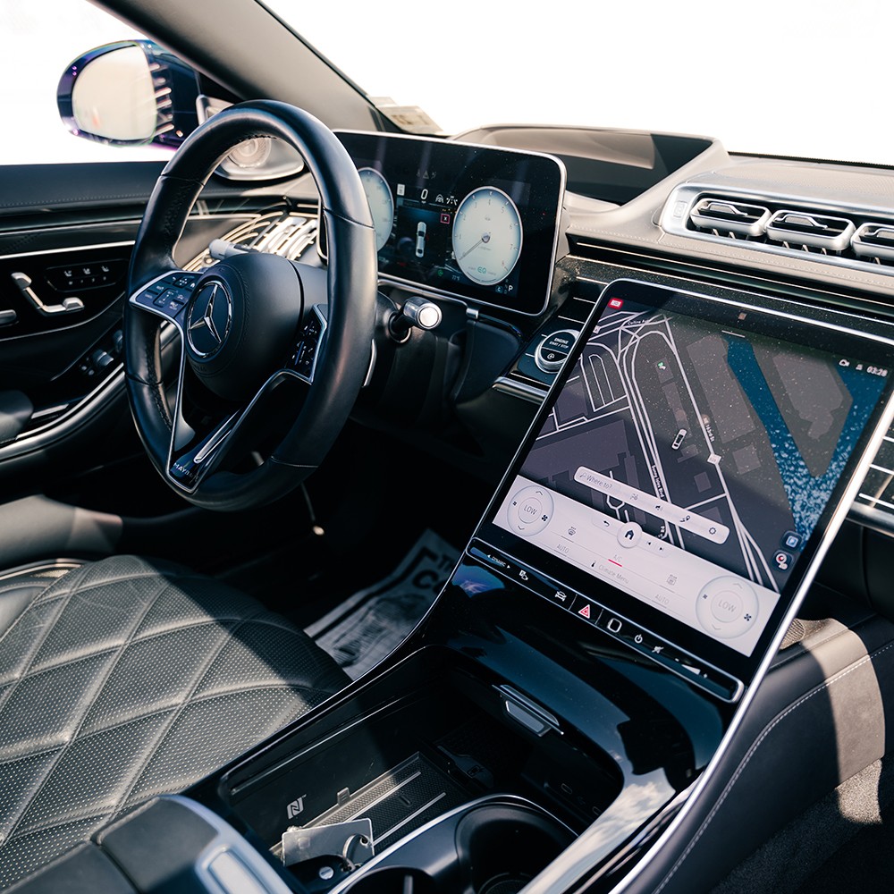 Driver's cockpit of the Mercedes-Maybach S580, featuring large digital displays, luxury steering wheel, and ambient lighting.