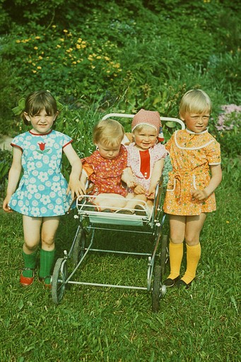 Neli väikest last vana lapsevankri ümber murul