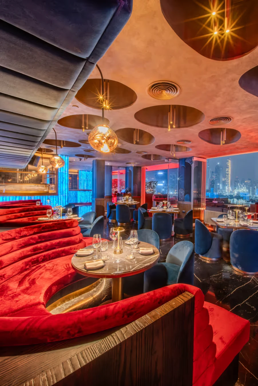 City View Lounge at The Penthouse Dubai with red velvet booths, blue velvet chairs and the Dubai Marina skyline through the windows