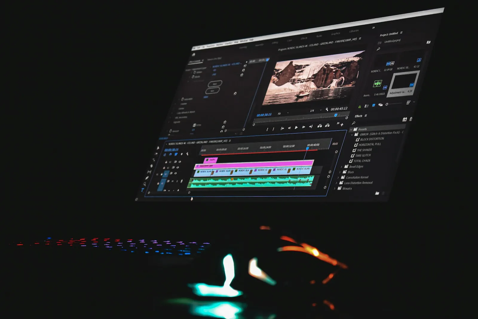 A monitor in a dark room shows video editing software with a preview window and a colourful clip timeline, beside a glowing keyboard and mouse