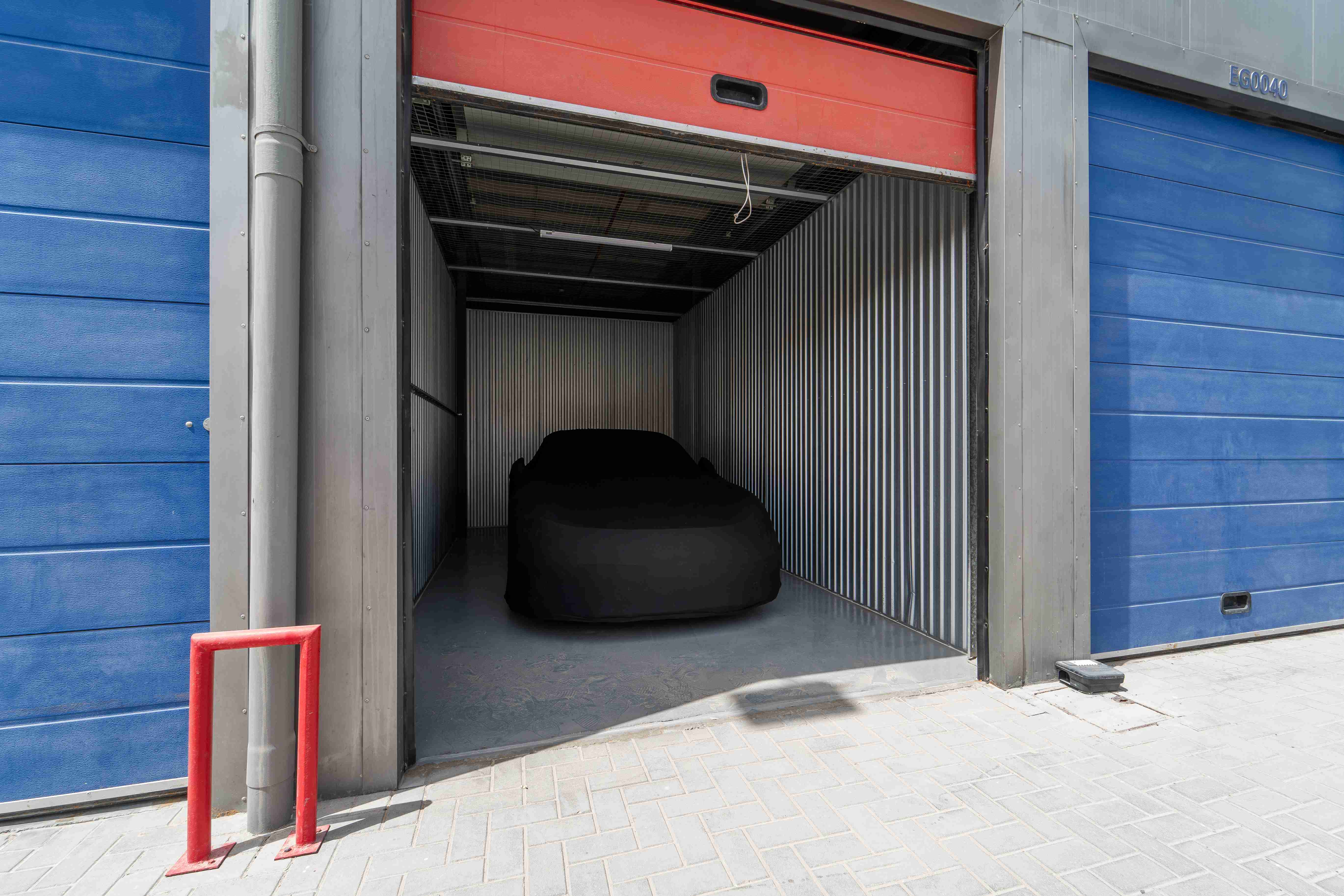 Covered car inside metal-walled unit with shutter door at a vehicle storage facility Dubai.