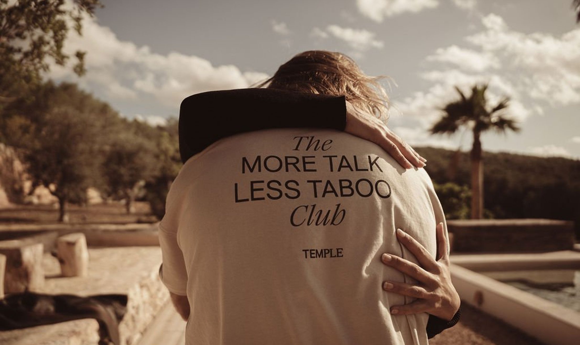 Couple hugging wearing More Talk Less Taboo Club shirt by Temple