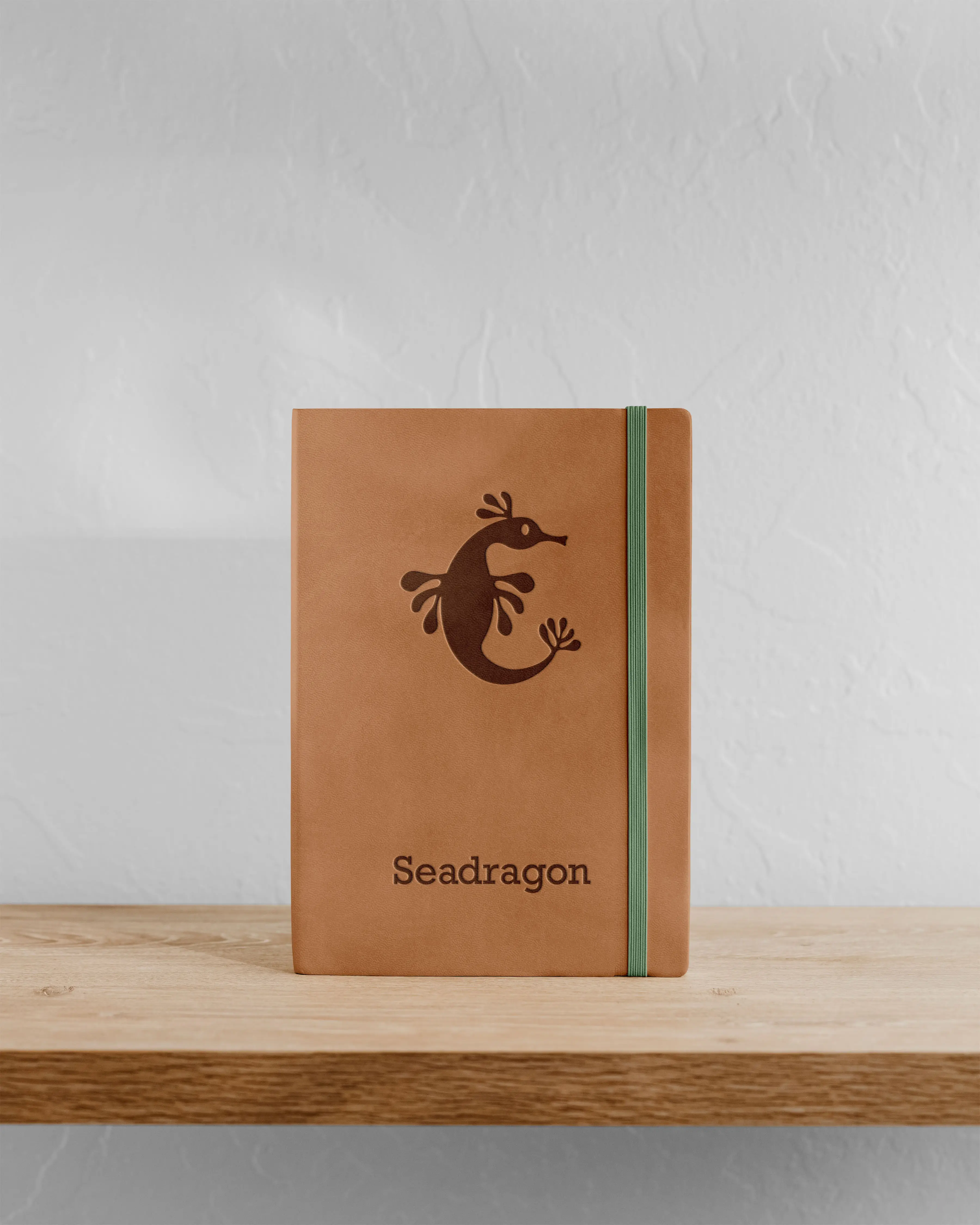A closed brown notebook with a stylized logo on the cover, placed on a wooden surface against a plain background.