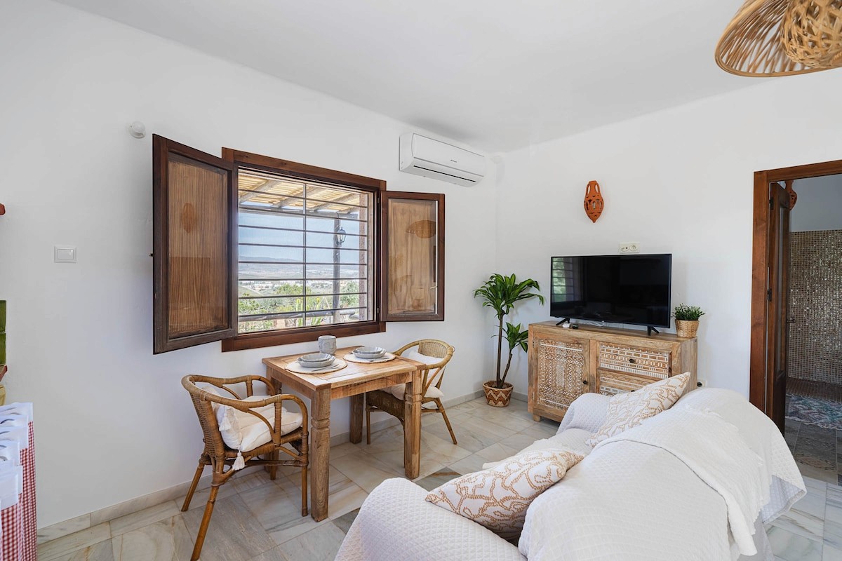 Salón luminoso de Luna Mora con sofá blanco, mesa de comedor y contraventanas de madera