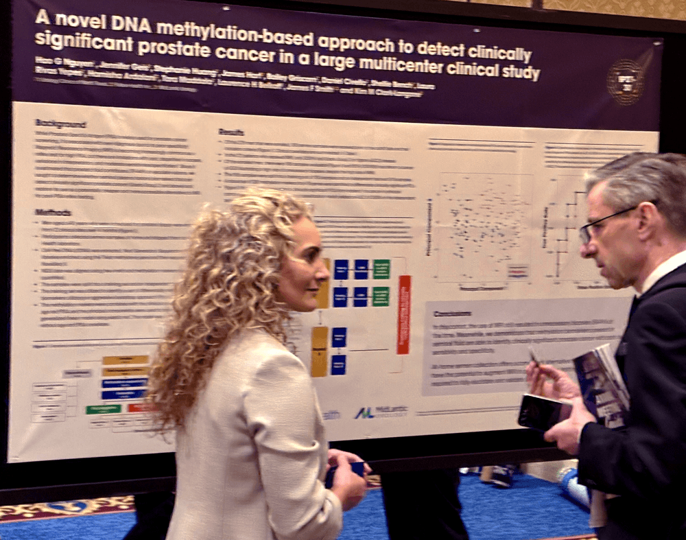 Two professionals stand in front of a research poster presented by Fellow