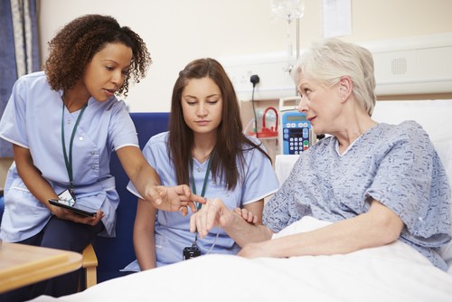 Two nurses attending to an elderly patient in a hospital bed, representing care staff training and competency tracking in healthcare settings