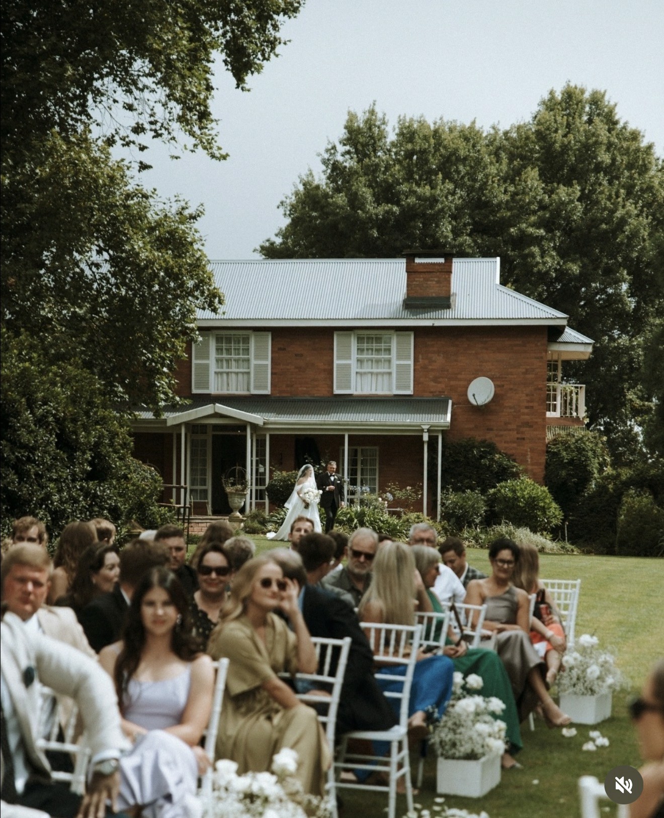 A serene outdoor wedding setup with white chairs arranged on green grass under a canopy of trees.
