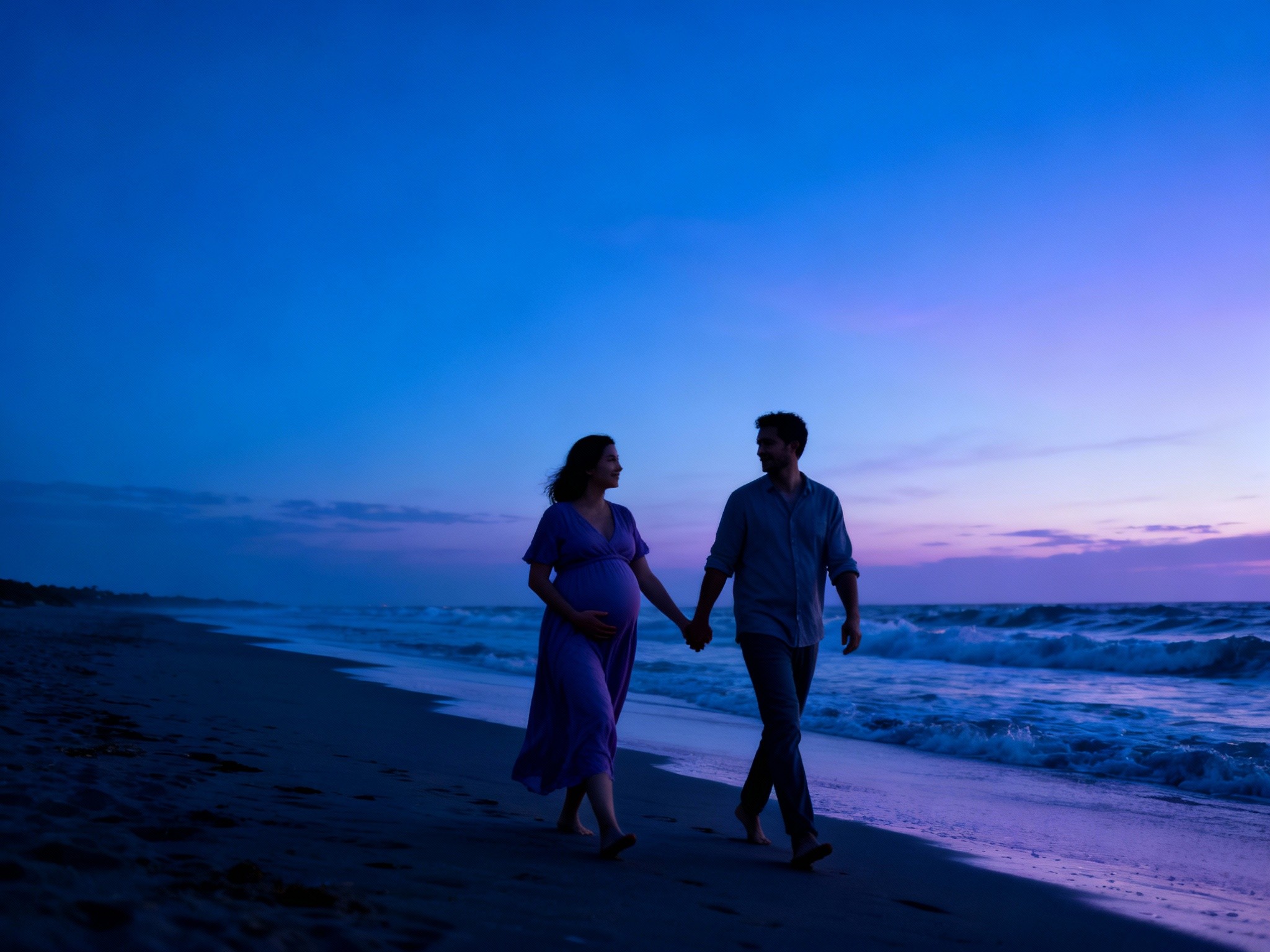 A dreamy twilight beach scene shows a pregnant couple walking hand in hand along the shoreline, the