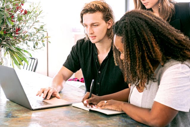 Two people sitting at a desk in front of a laptop