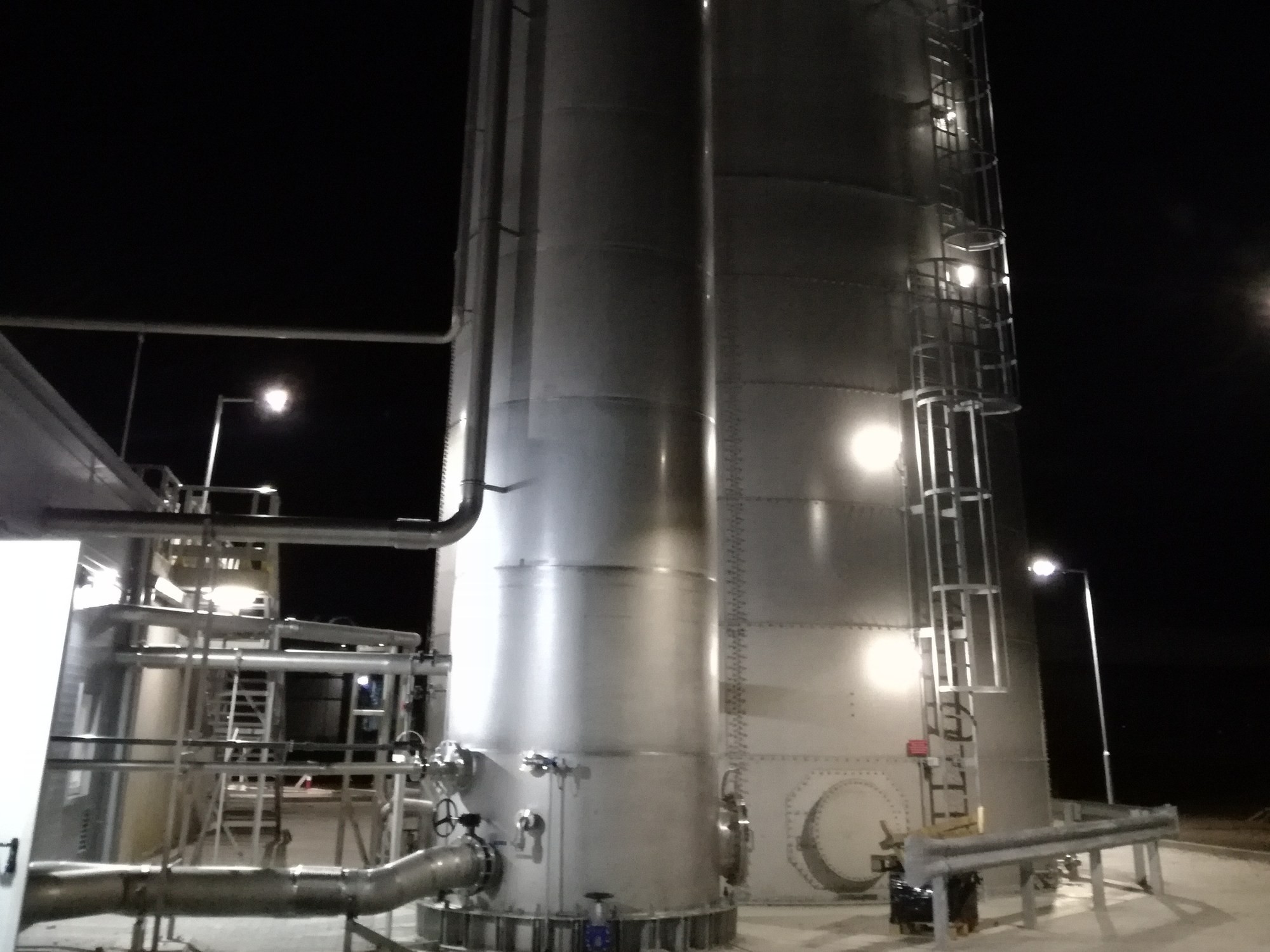 Stainless-steel reactor tower lit at night at the Kall Ingredients wastewater treatment plant, Tiszapüspöki, Hungary