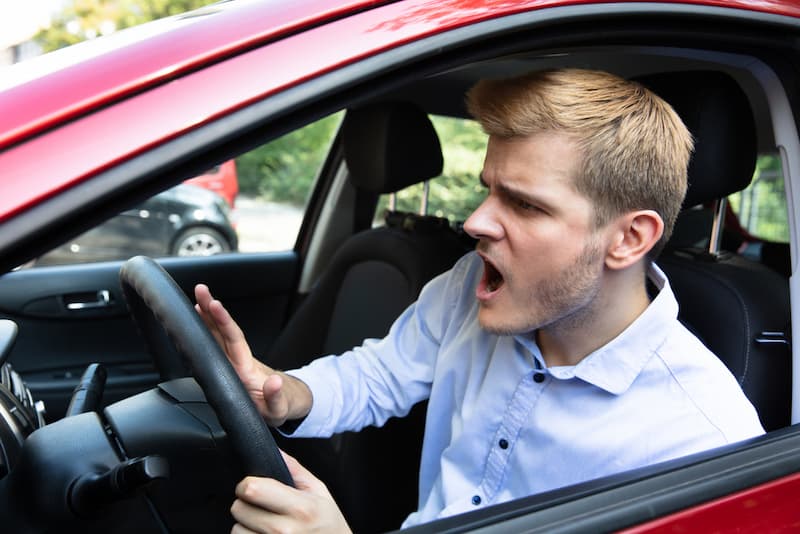 a young adult in the driver seat of a vehicle, on the horn, visibly frustrated with (likely) another vehicle